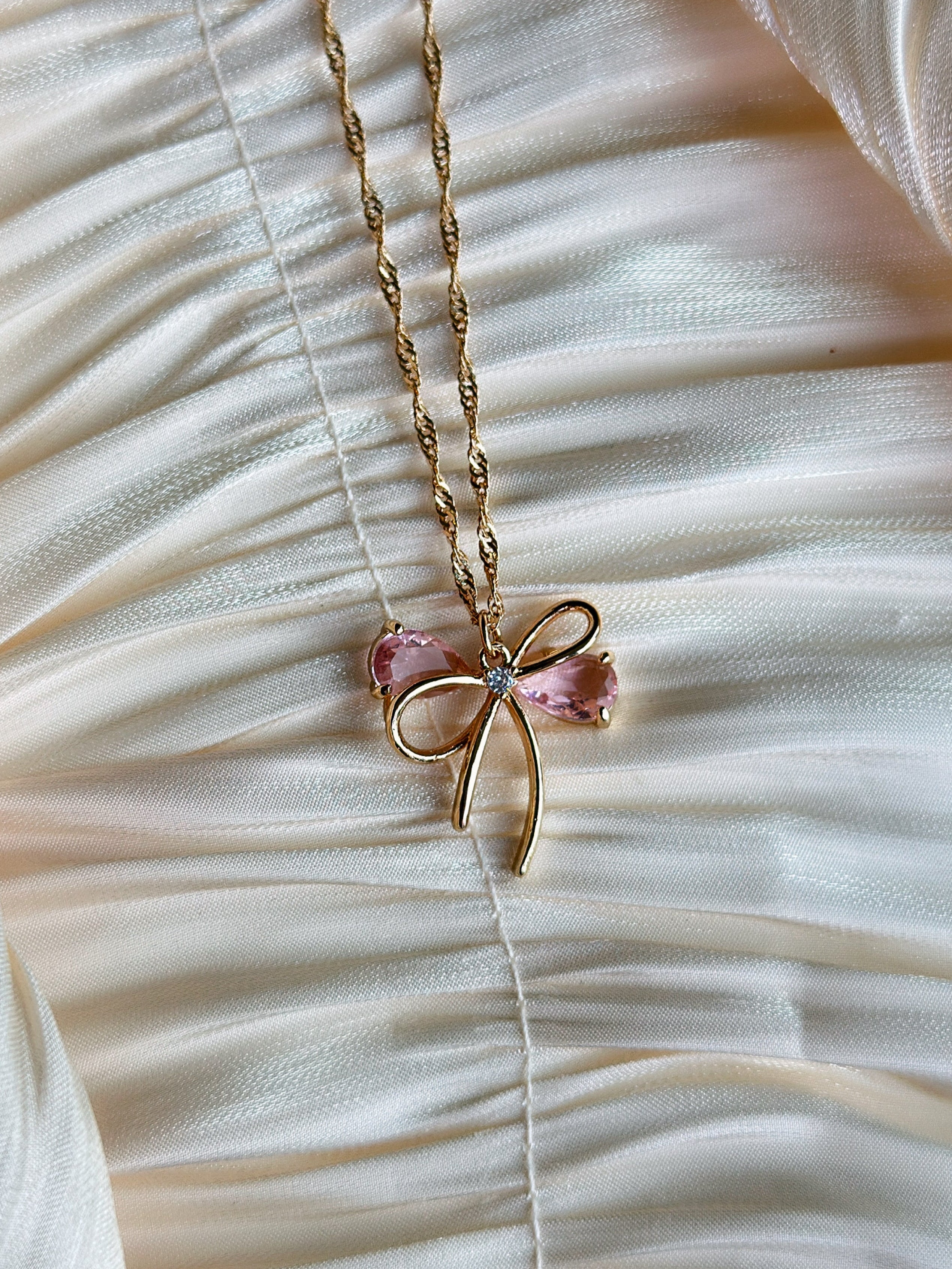 Gold bow pendant necklace with pink gemstone accents on a twisted gold chain.