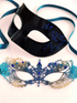 Couple’s masquerade mask set with a teal and gold lace rhinestone women’s mask and a sleek black men’s mask with blue scrollwork.