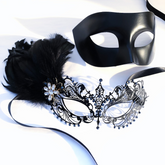 Black couples masquerade mask set with matte black men’s mask and filigree women’s mask with feathers, rhinestones, and jewel accent.