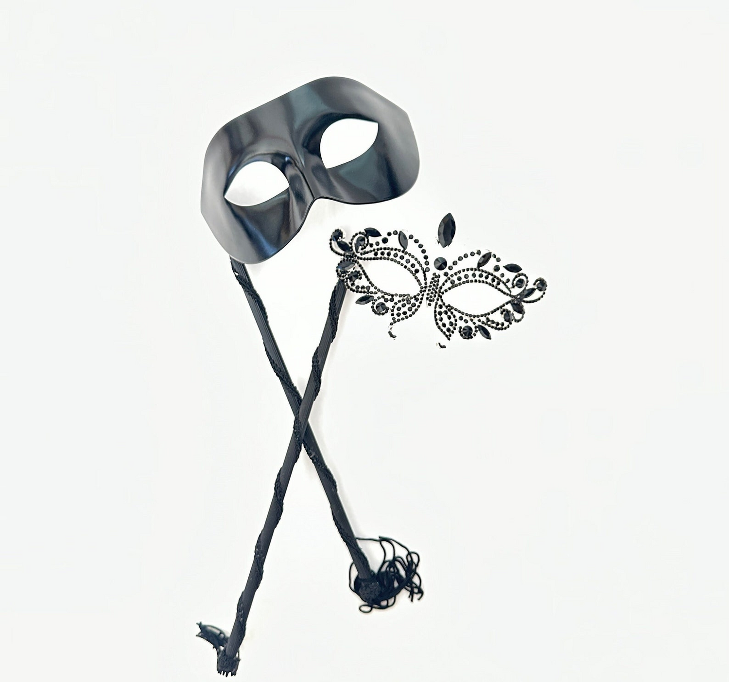 Black phantom-style men’s masquerade mask on stick with matching women’s rhinestone filigree mask, designed for elegant couple’s wear.