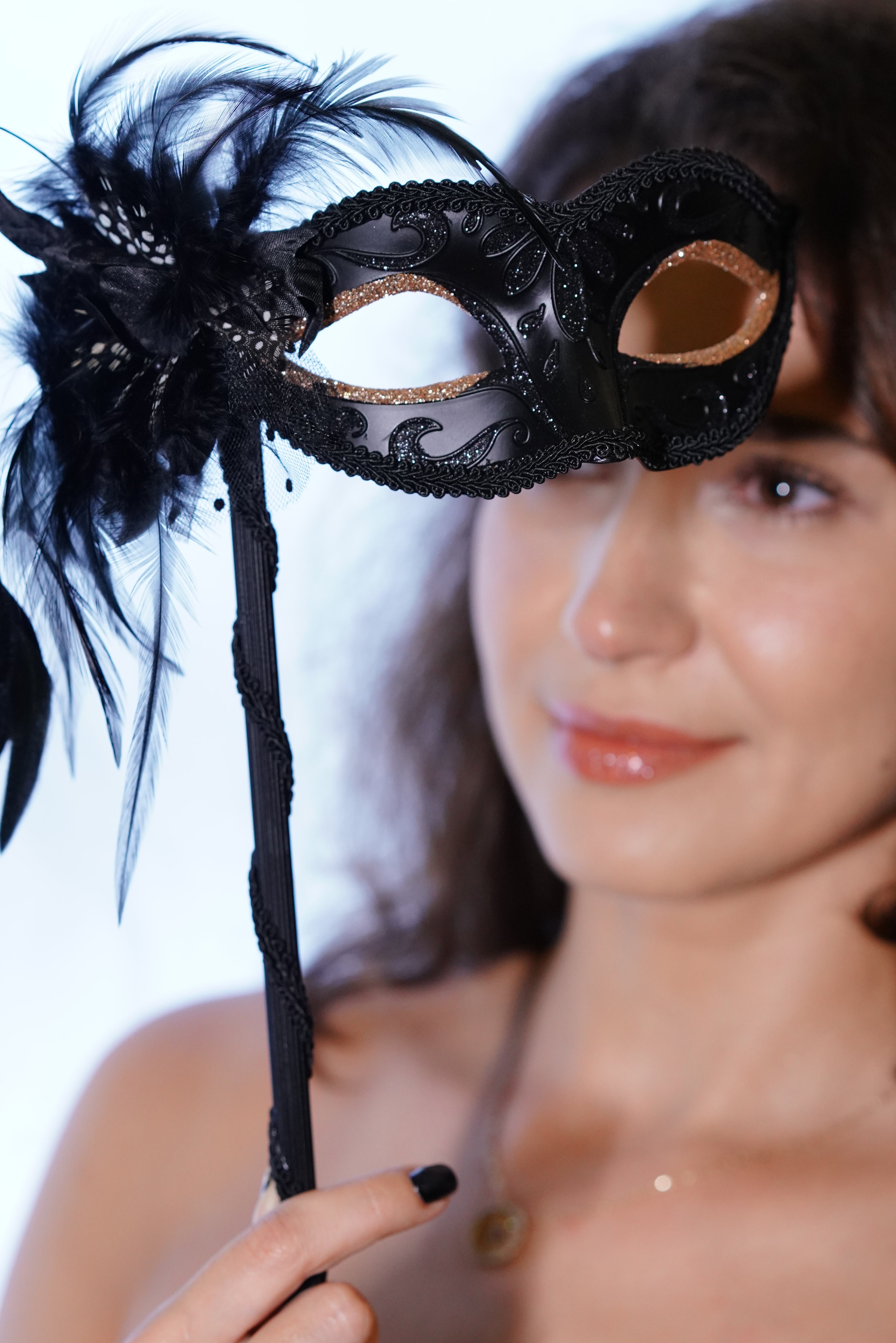 Woman holding a handheld black masquerade mask with feathers and lace trim.