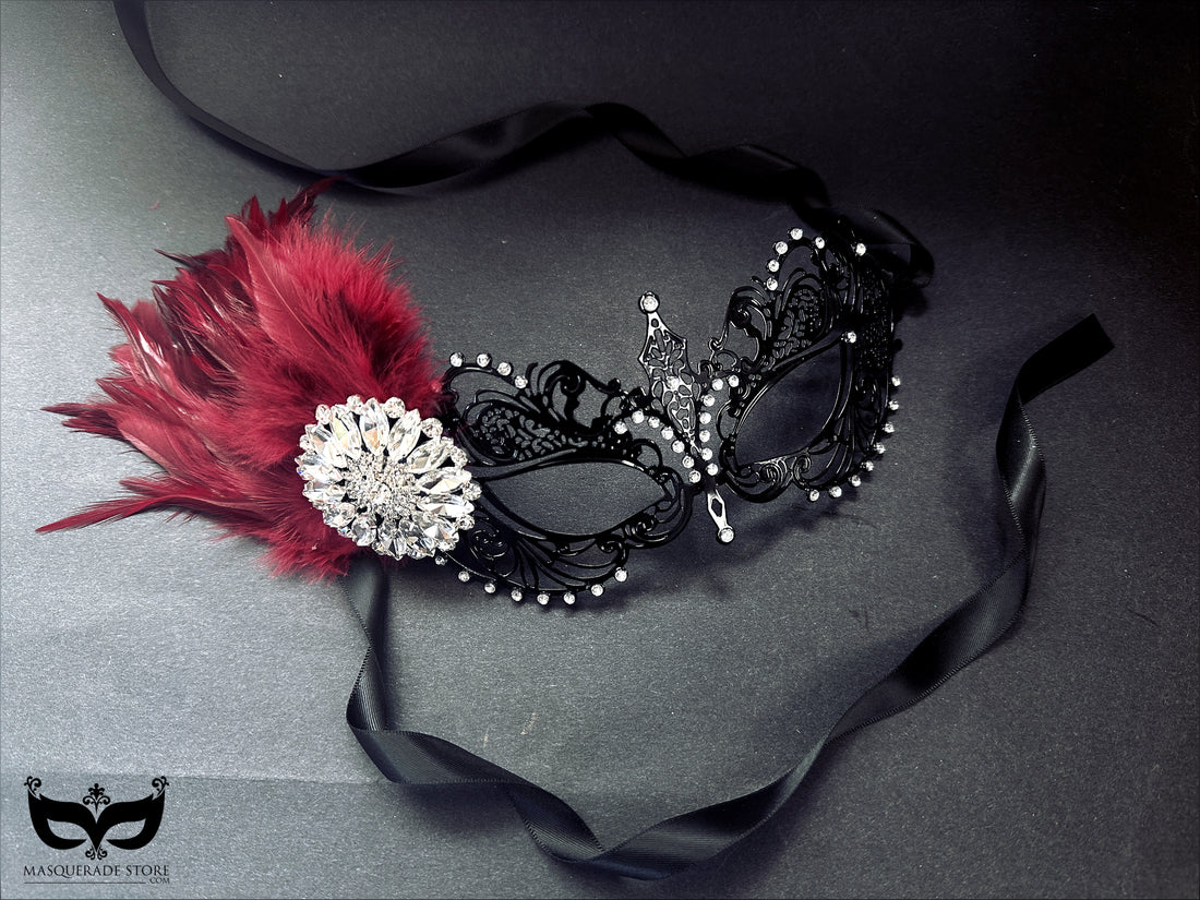 Black metal masquerade mask with burgundy feathers and rhinestone jewel, perfect for Mardi Gras and masquerade balls