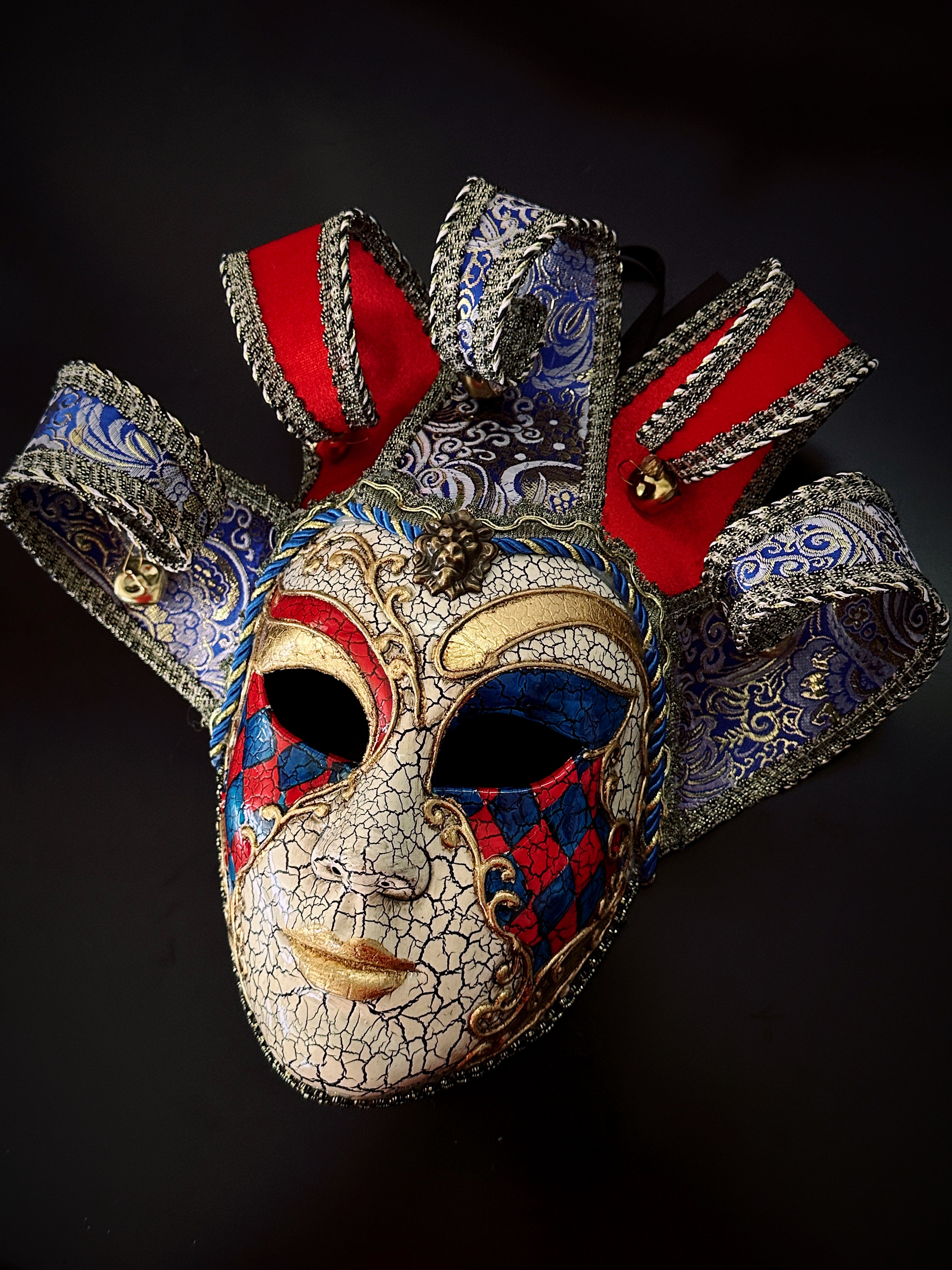 Venetian harlequin jester mask with red, blue, and gold diamond design and curled horns.