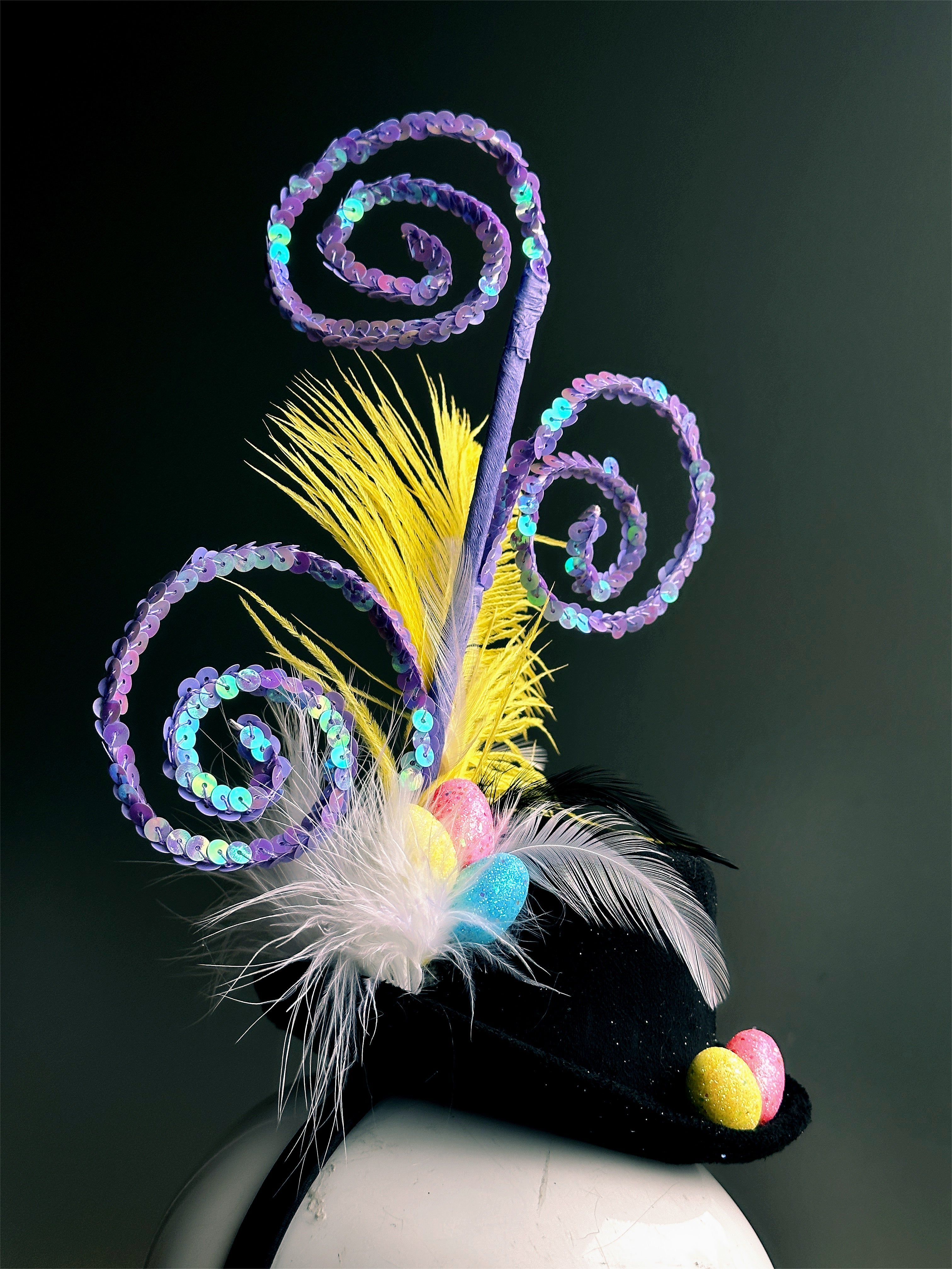 Black mini hat fascinator with yellow feather, purple spirals, and colorful Easter egg accents