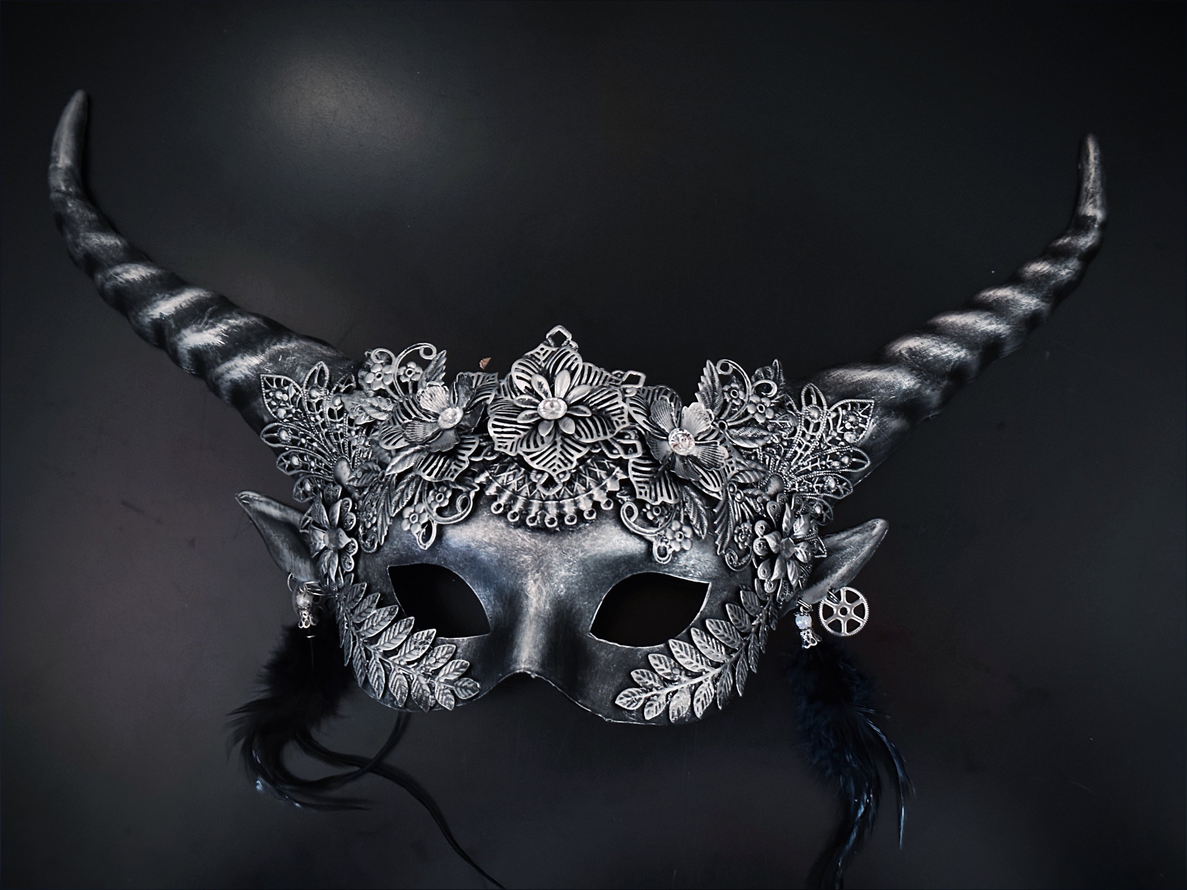 Silver fantasy horn masquerade mask with floral filigree, black feathers, elf ears, and steampunk gears