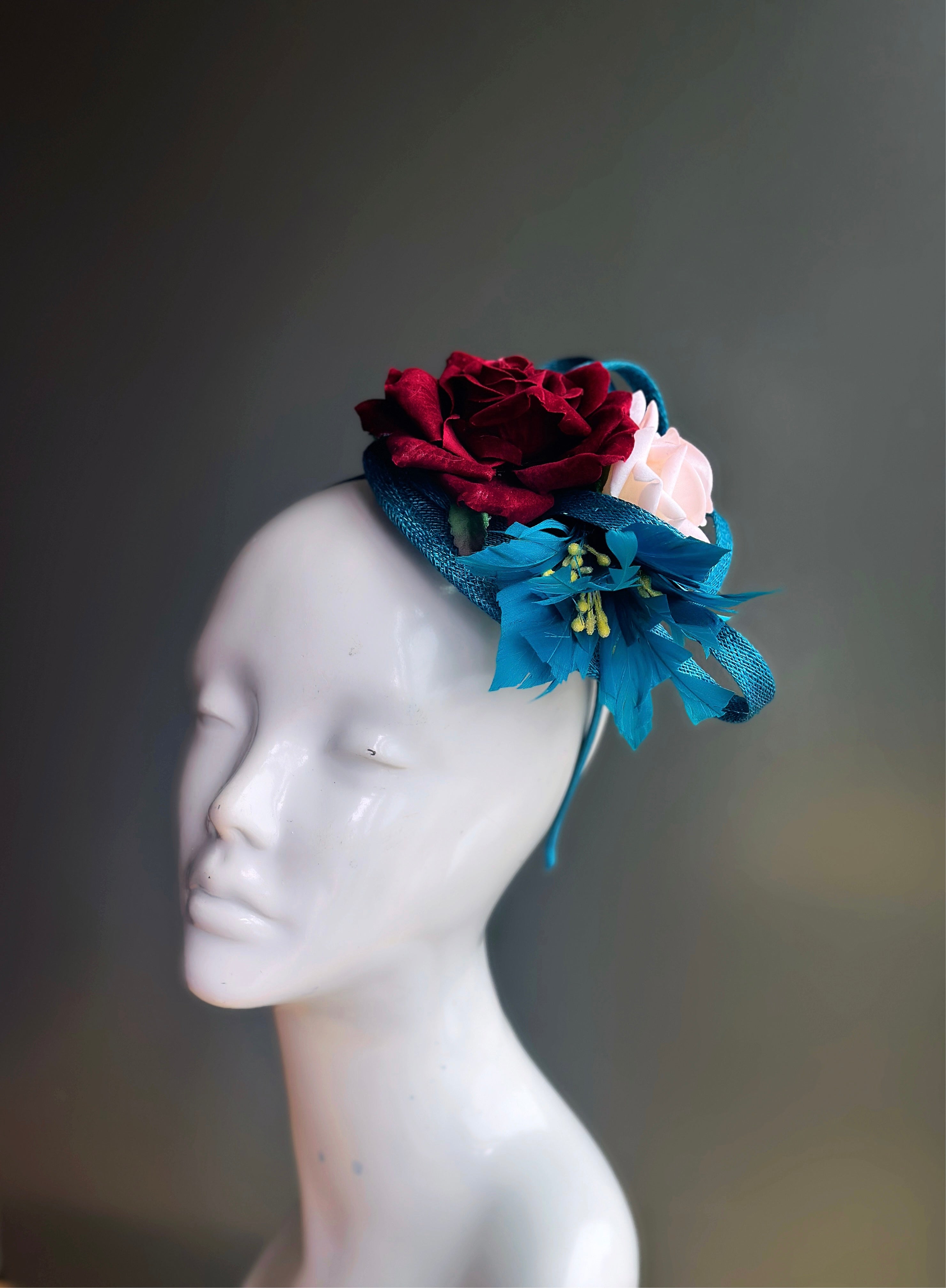 Fascinator hat with a teal base and red and white roses.