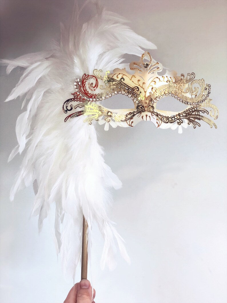Handheld Venetian mask with white feathers, gold trim, and sparkling rhinestones.