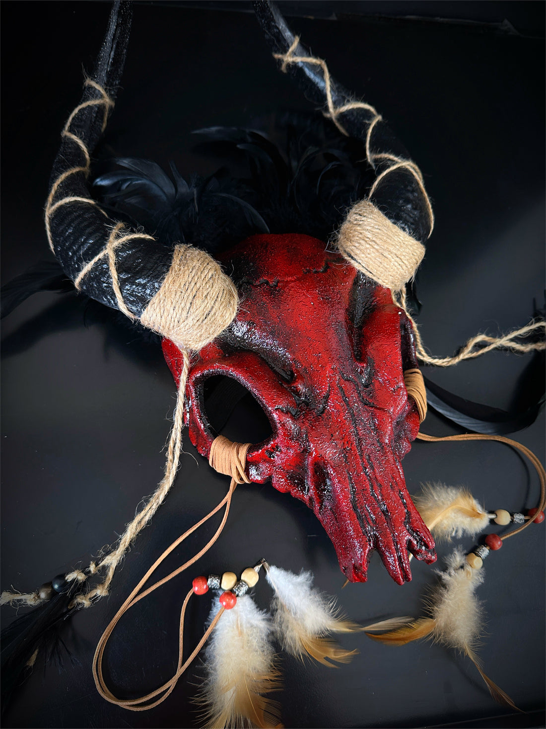 Ram skull horn headdress in blood red with black feathers.
