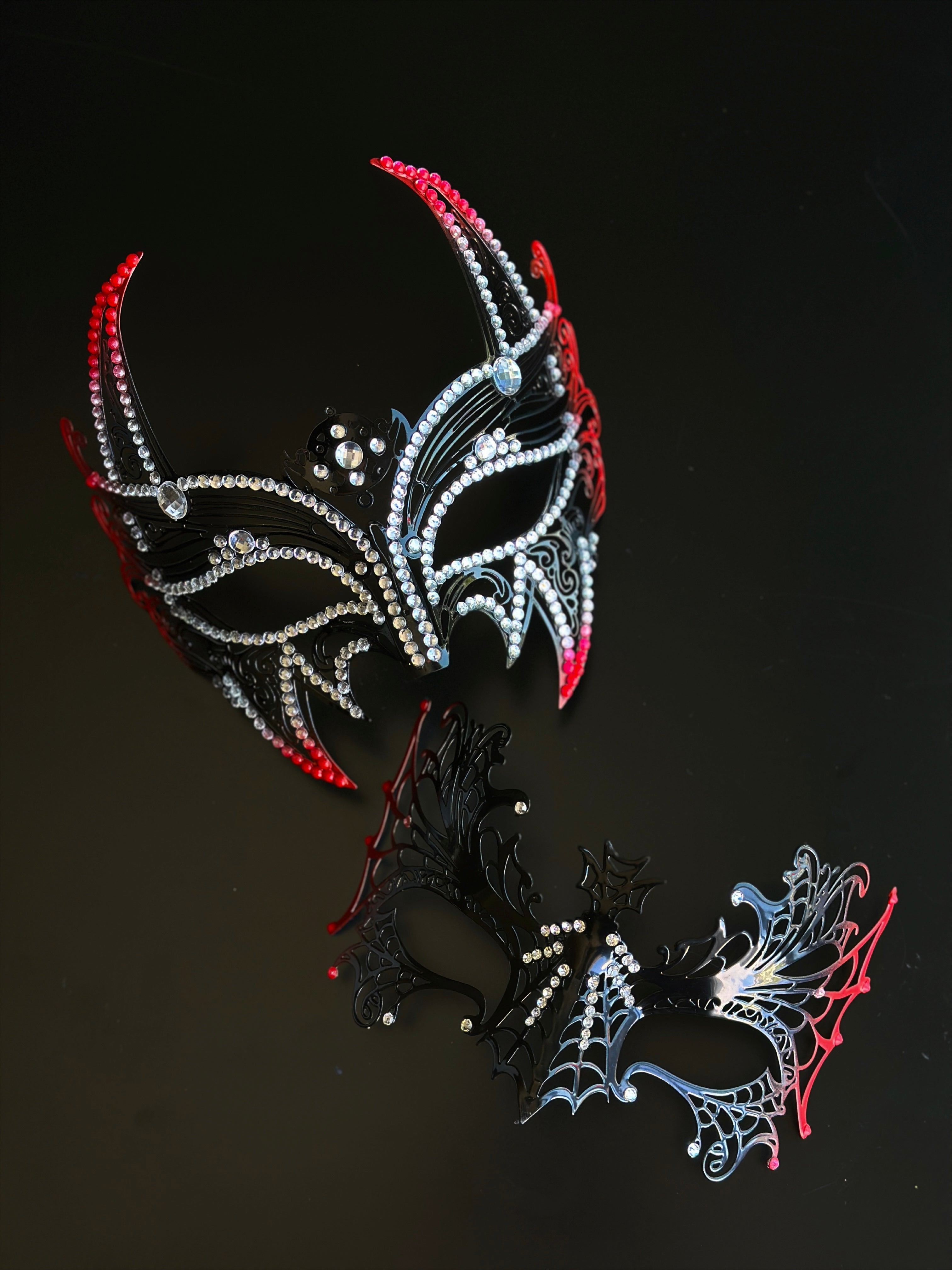 Red and black couples masquerade mask set with a horned rhinestone masquerade mask and a spiderweb-style eye mask for gothic formal events.