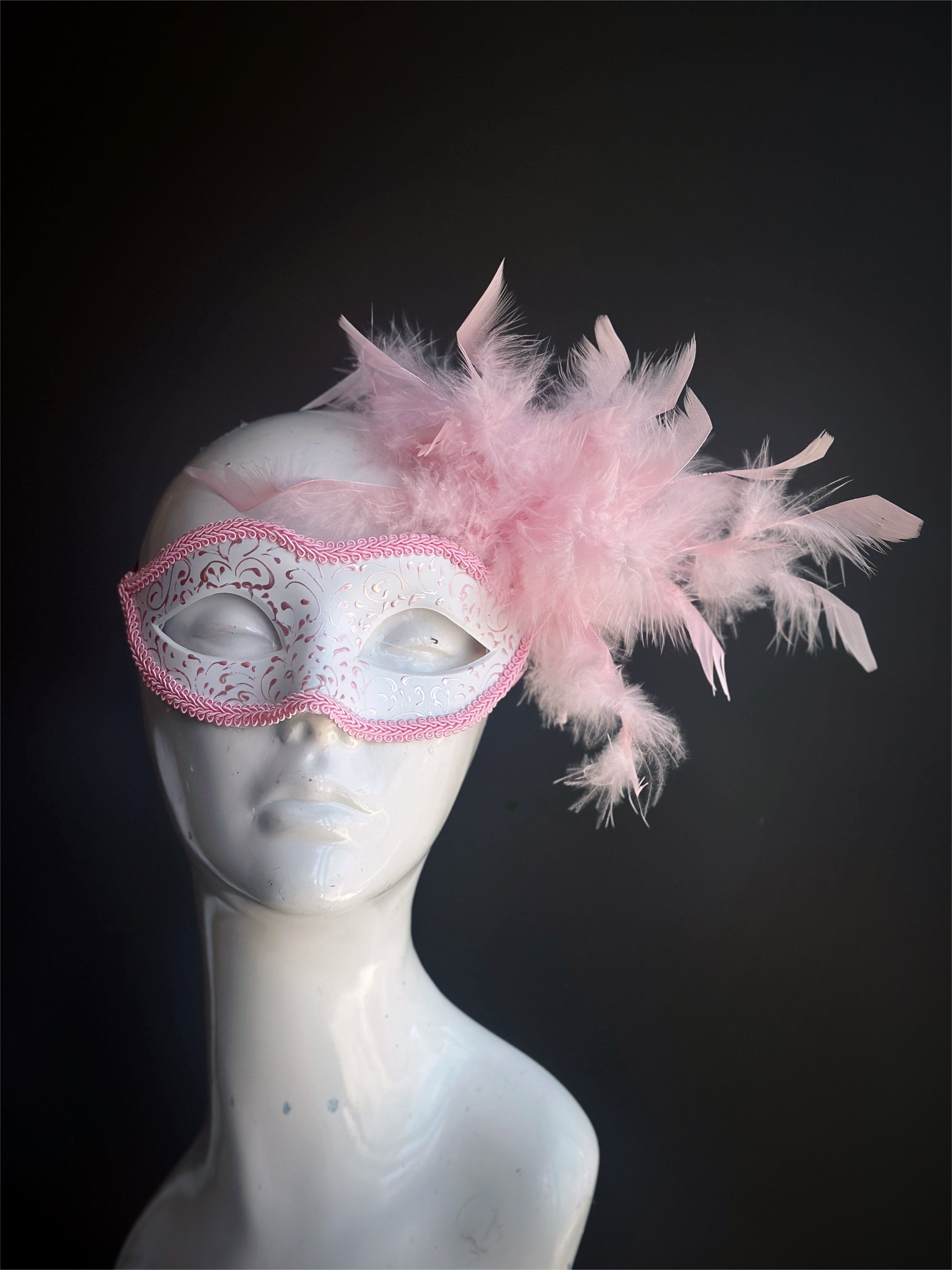 Elegant masquerade mask in pink and white with soft feathers and glittery accents, perfect for sweet and feminine party looks.