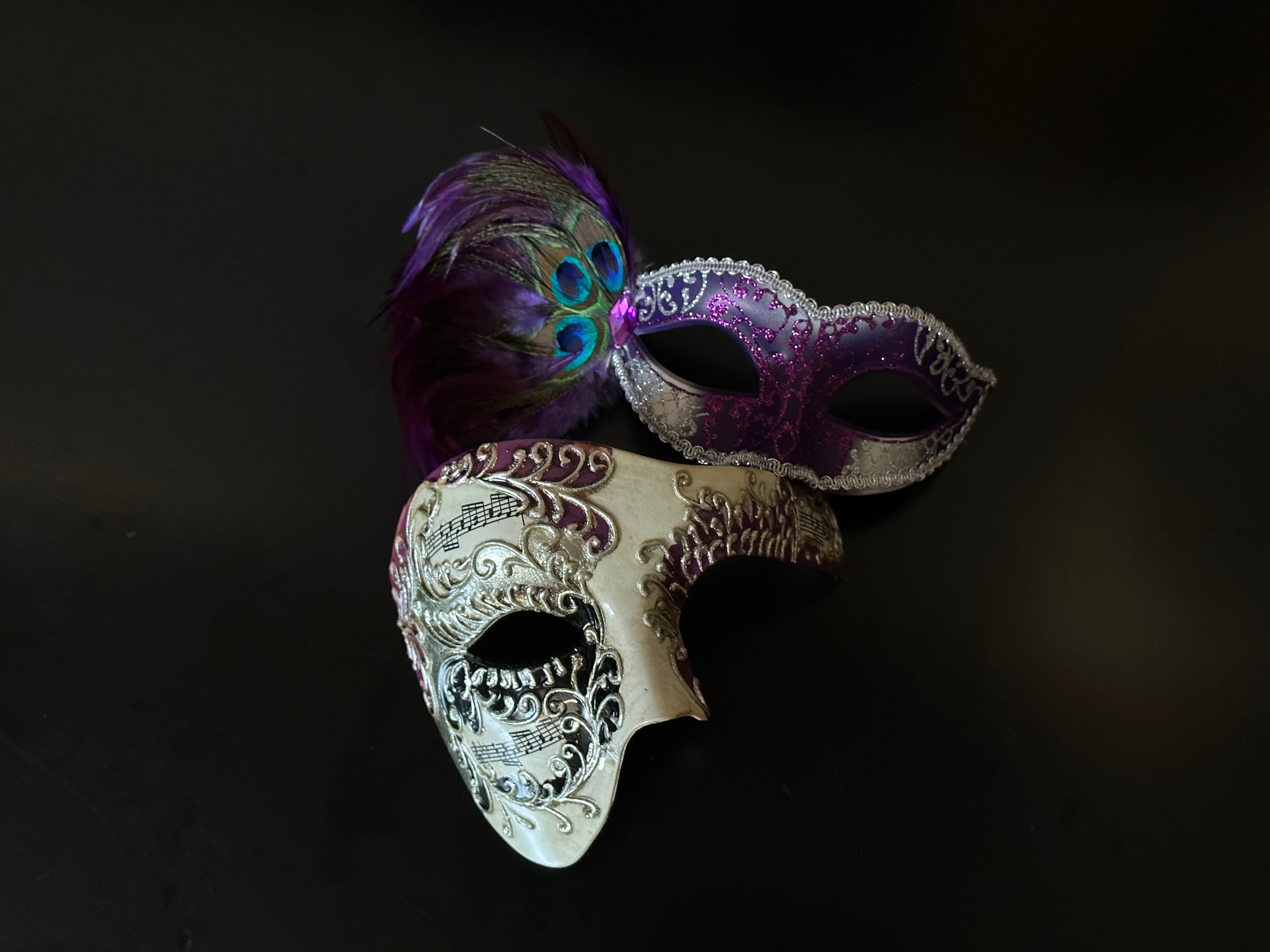 Purple and ivory masquerade mask set for couples with peacock feathers, glitter swirls, and vintage musical scroll details.