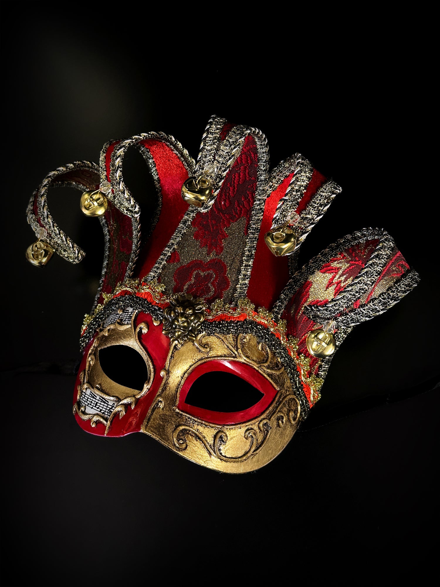 Elegant jester mask with red fabric points, gold trim, and festive details, perfect for masquerade events