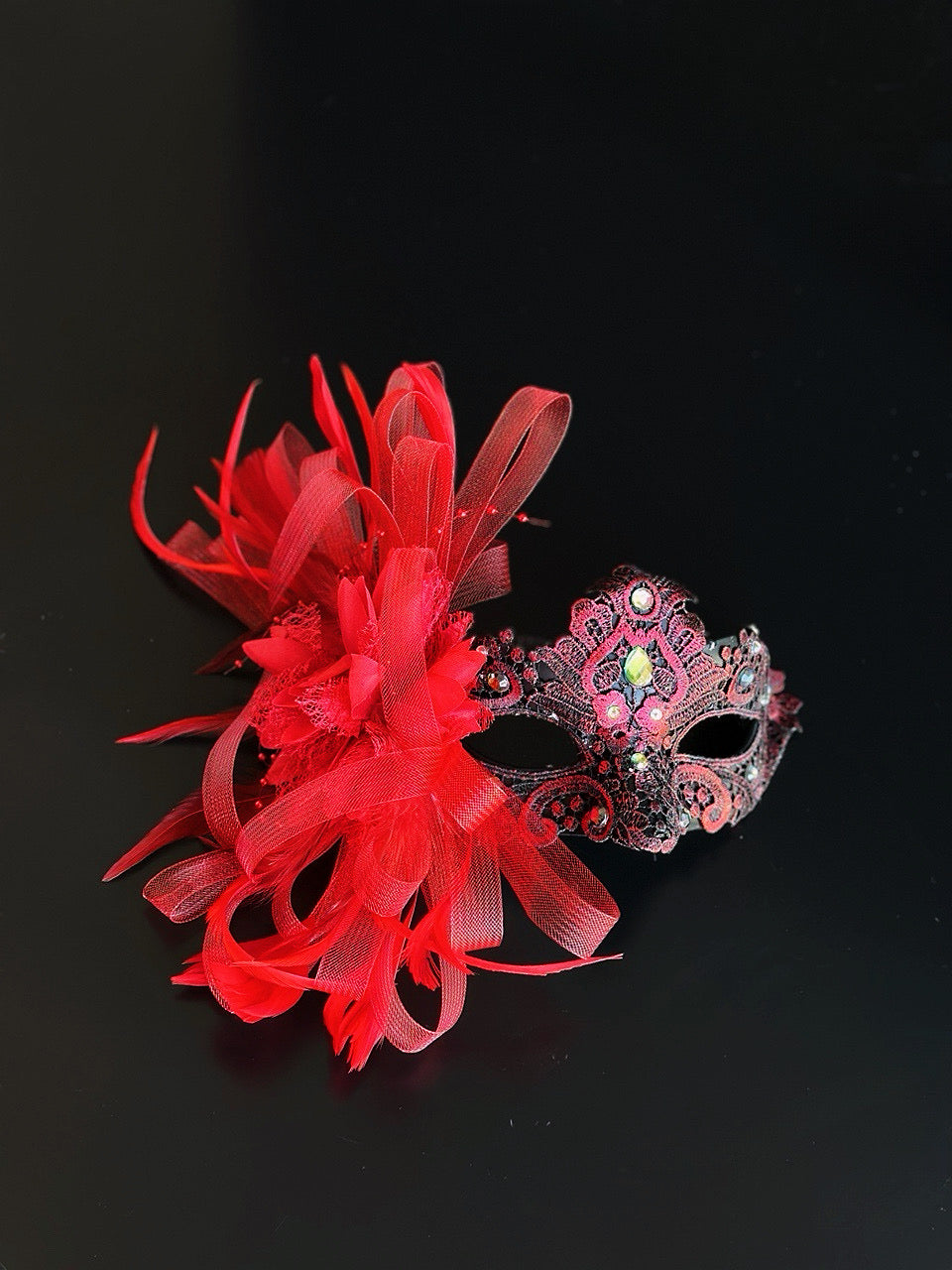 Red lace masquerade mask with feather flower and crystal details for gala and formal masquerade events.