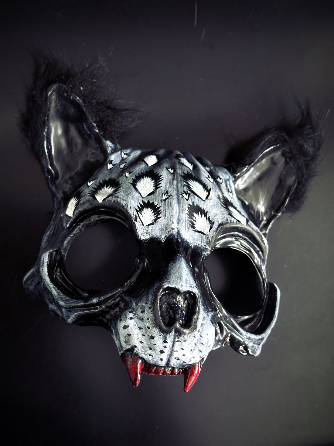 Silver and black wildcat masquerade mask with fur ears, spotted pattern, and red fangs for Halloween or cosplay.