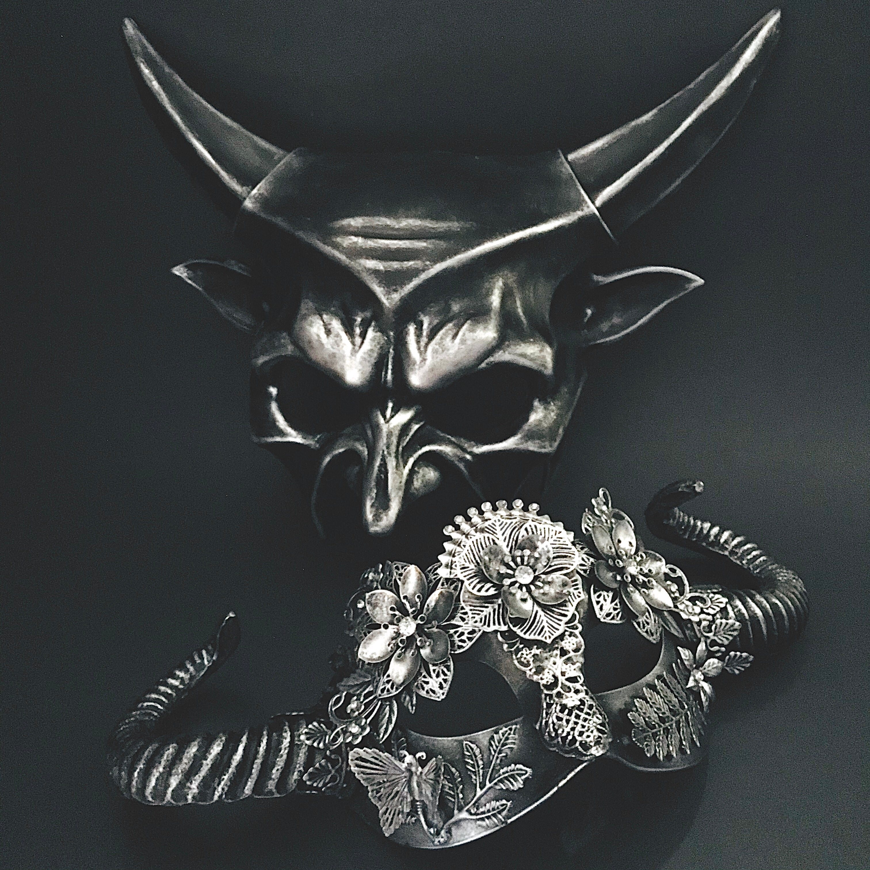 Gothic silver masquerade mask pair featuring sculpted horns, filigree flowers, and fantasy-inspired details.