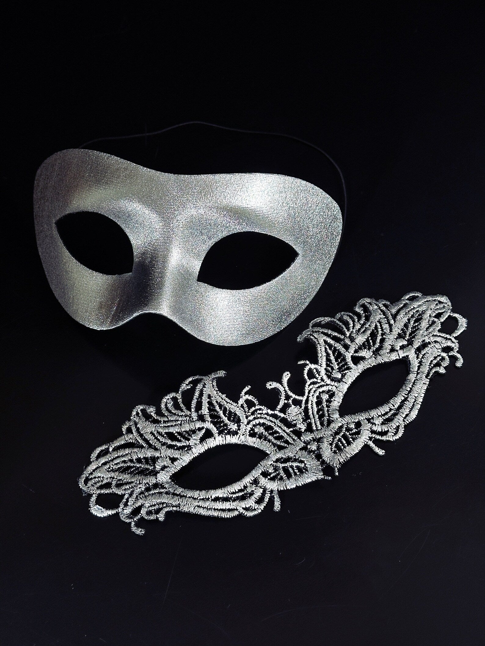 Silver metallic couples masquerade masks featuring a sleek men’s mask and a delicate lace women’s mask, ideal for Venetian balls, weddings, and formal celebrations.
