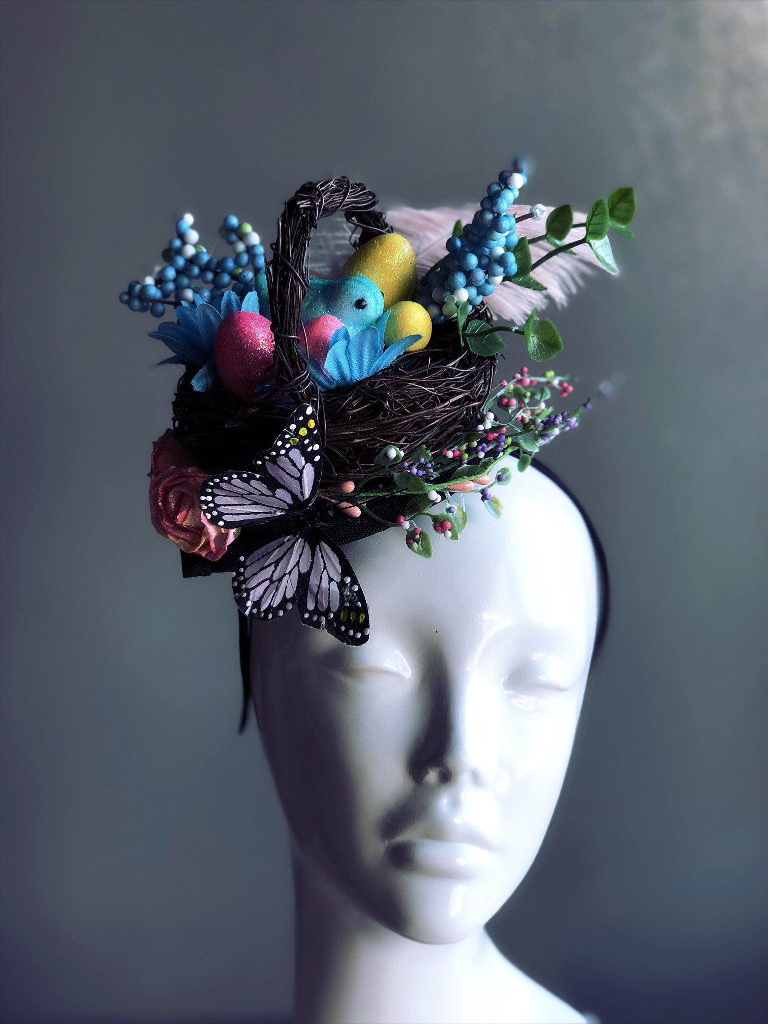 Easter themed fascinator with a woven basket full of Easter eggs, colored peeps, butterflies, feathers and floral accents attached on a headband