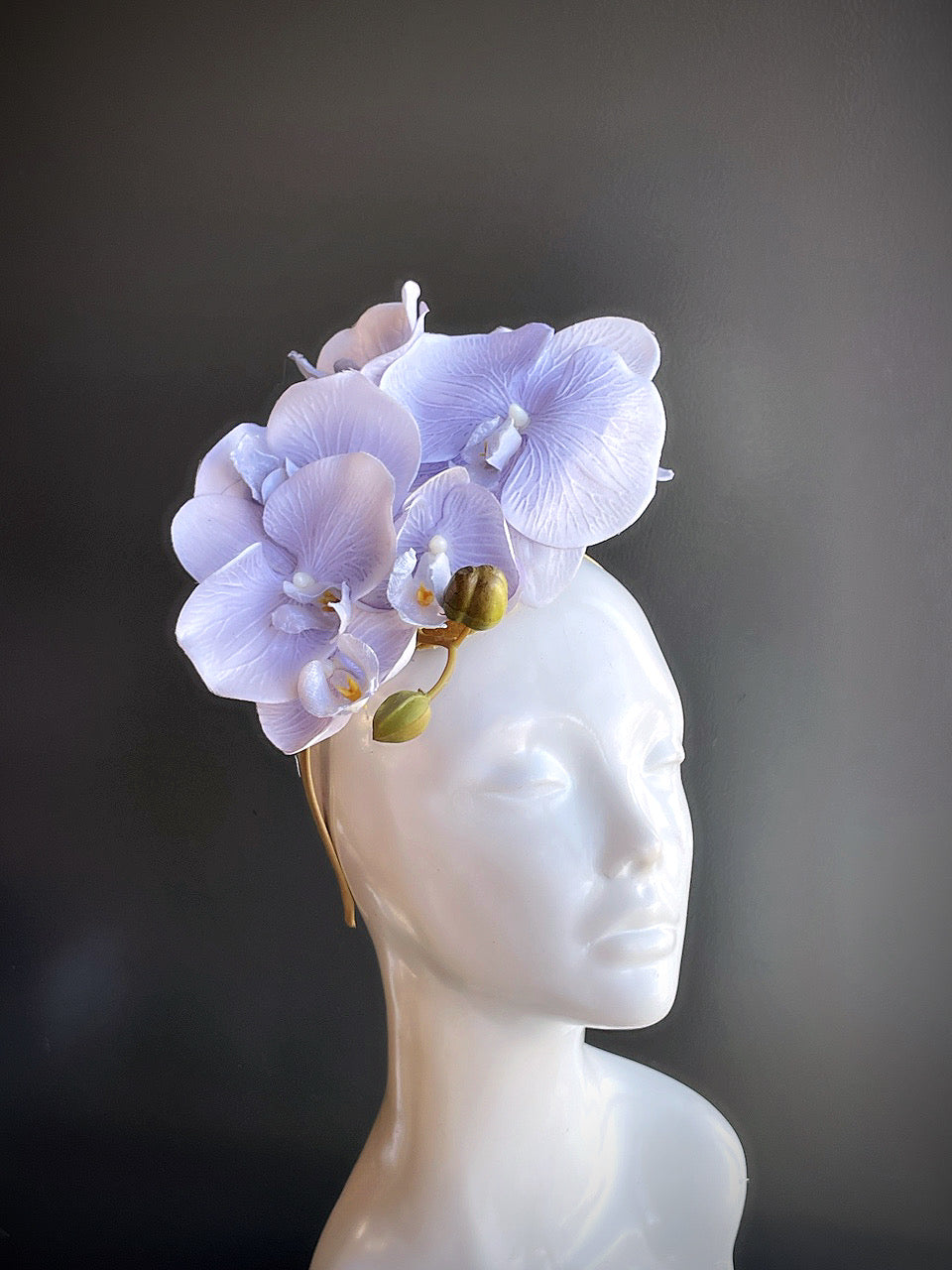 Lavender orchid fascinator with a gold base displayed on a mannequin head.