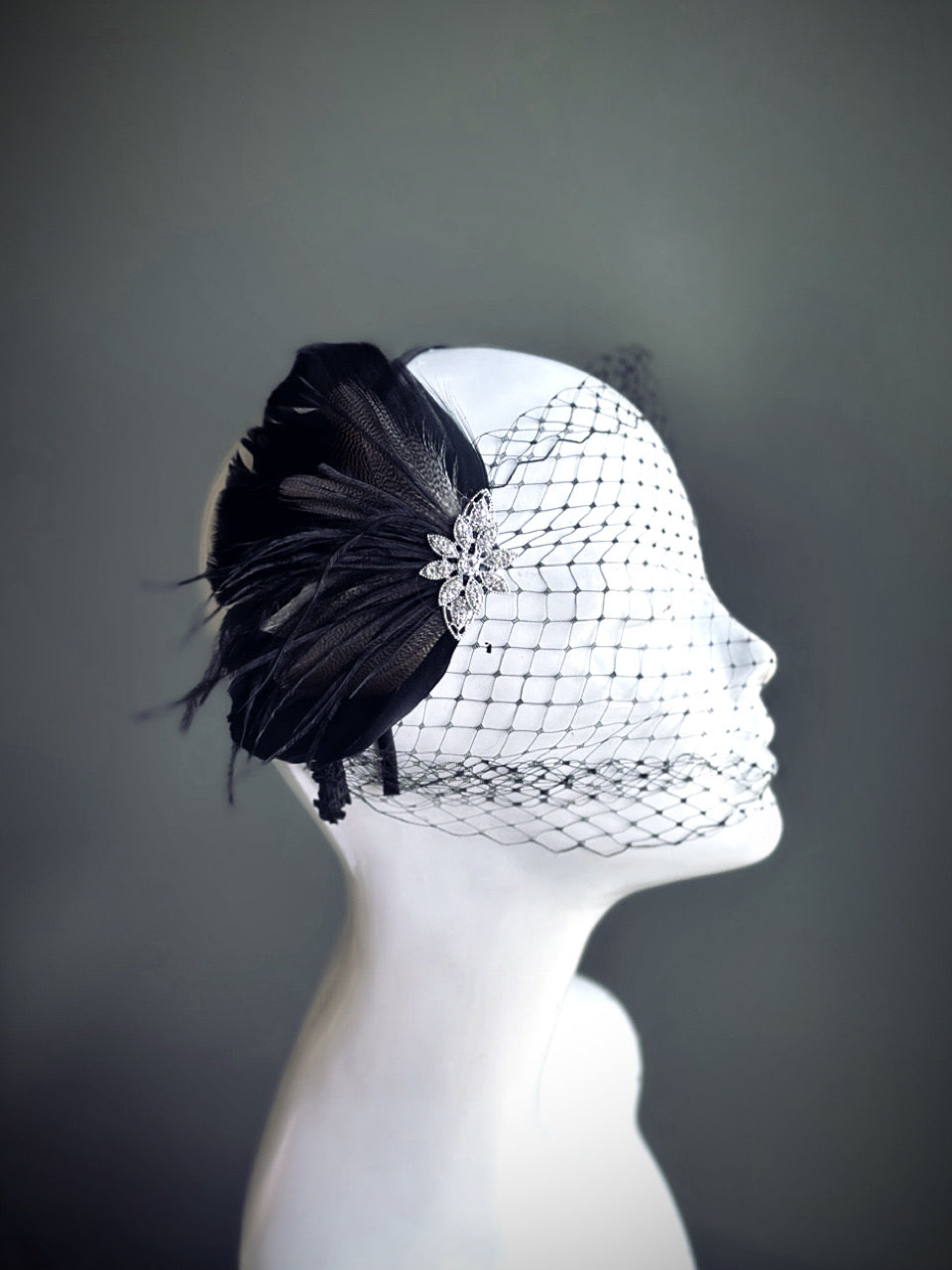 "Black feather fascinator with a rhinestone accent and dotted mesh veil, perfect for weddings and formal occasions."
