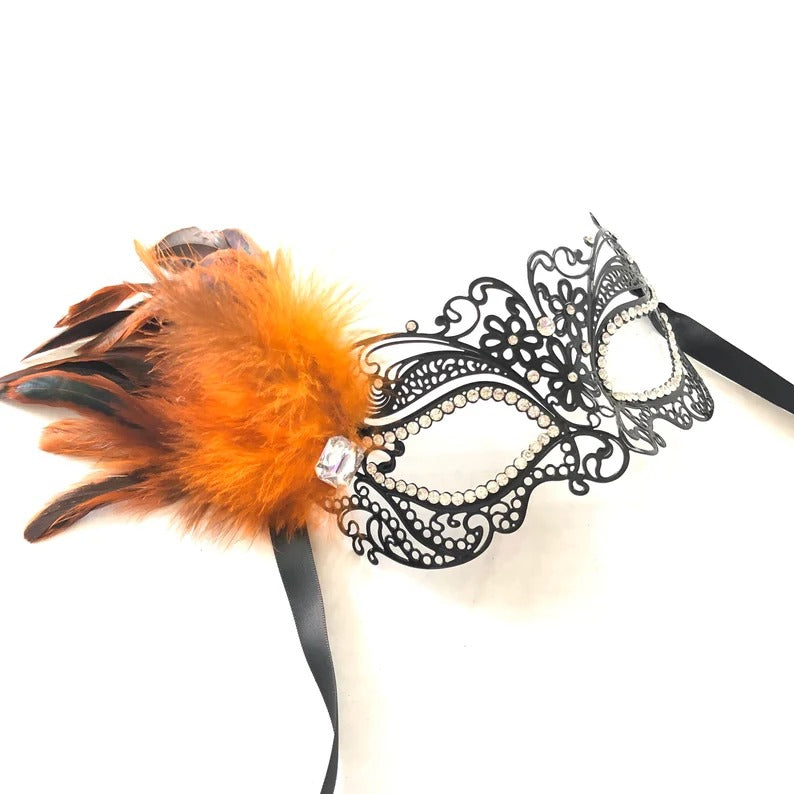 Elegant black filigree masquerade mask with bright orange feathers and rhinestone details.