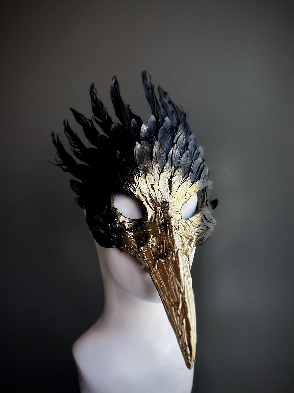 Black and gold bird mask with sculpted feather details and a long beak, perfect for masquerades, fantasy events, and theatrical performances.