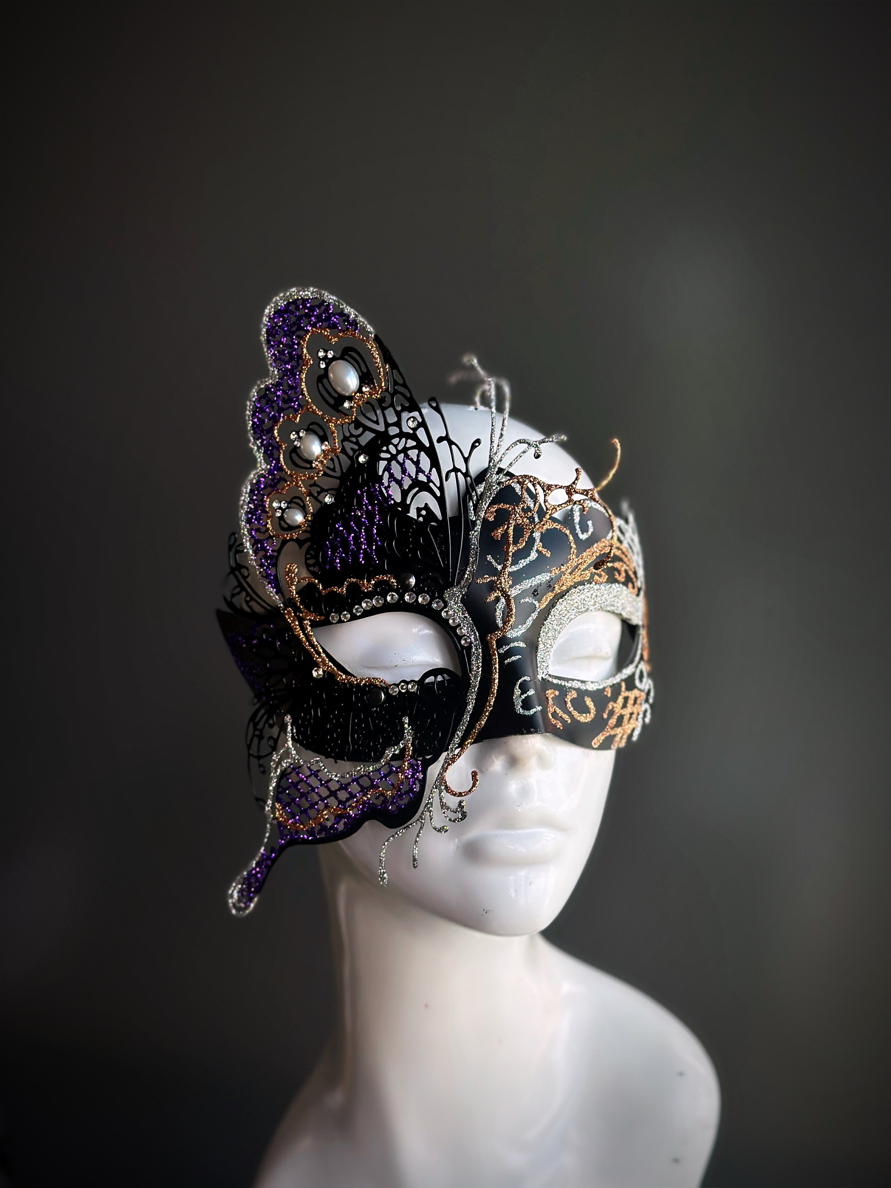 Black and gold masquerade mask with a purple butterfly accent and rhinestone details displayed on a mannequin head.