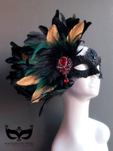 Black lace masquerade mask with green and gold feathers and red brooch for women.