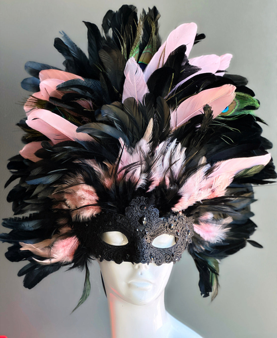 Black lace masquerade mask with pink, black, and peacock feathers in a grand plume.