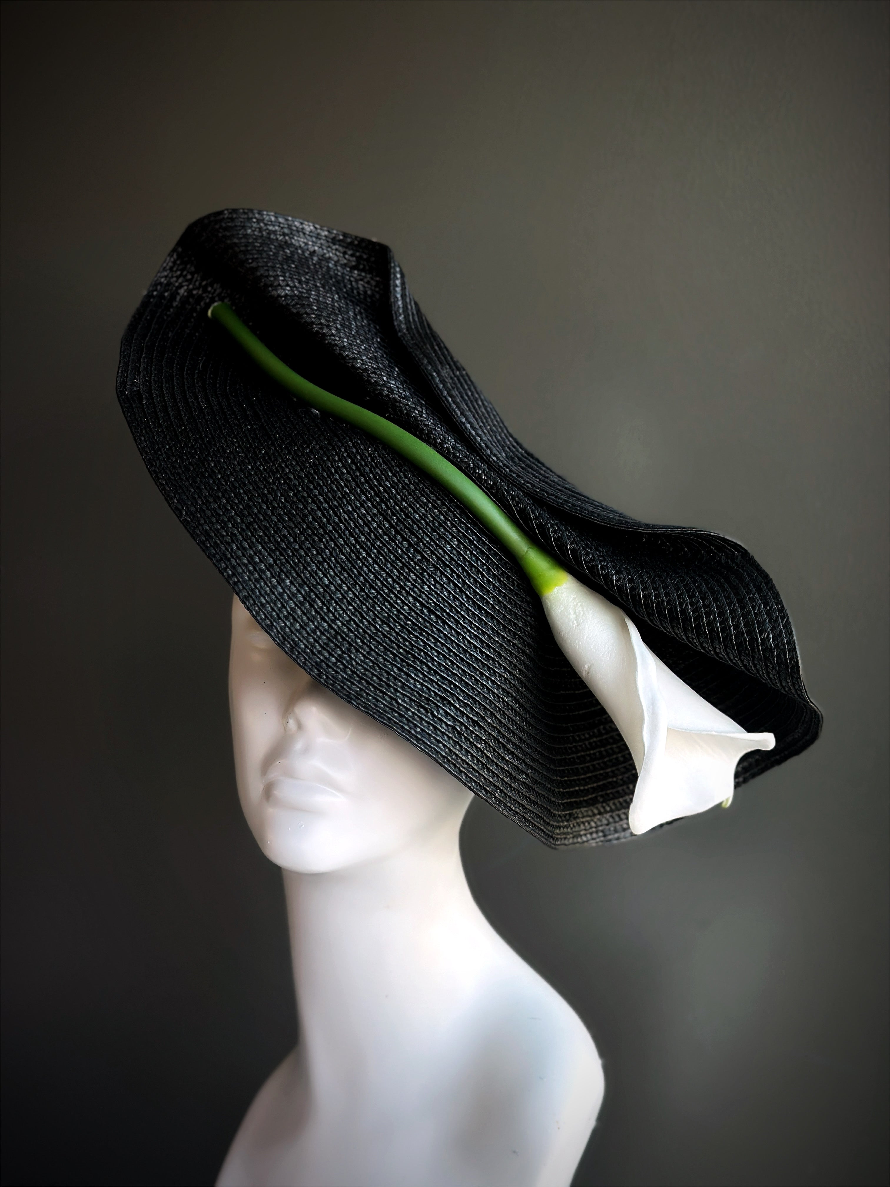 Black fascinator hat with sculptural design and white tulip accent.