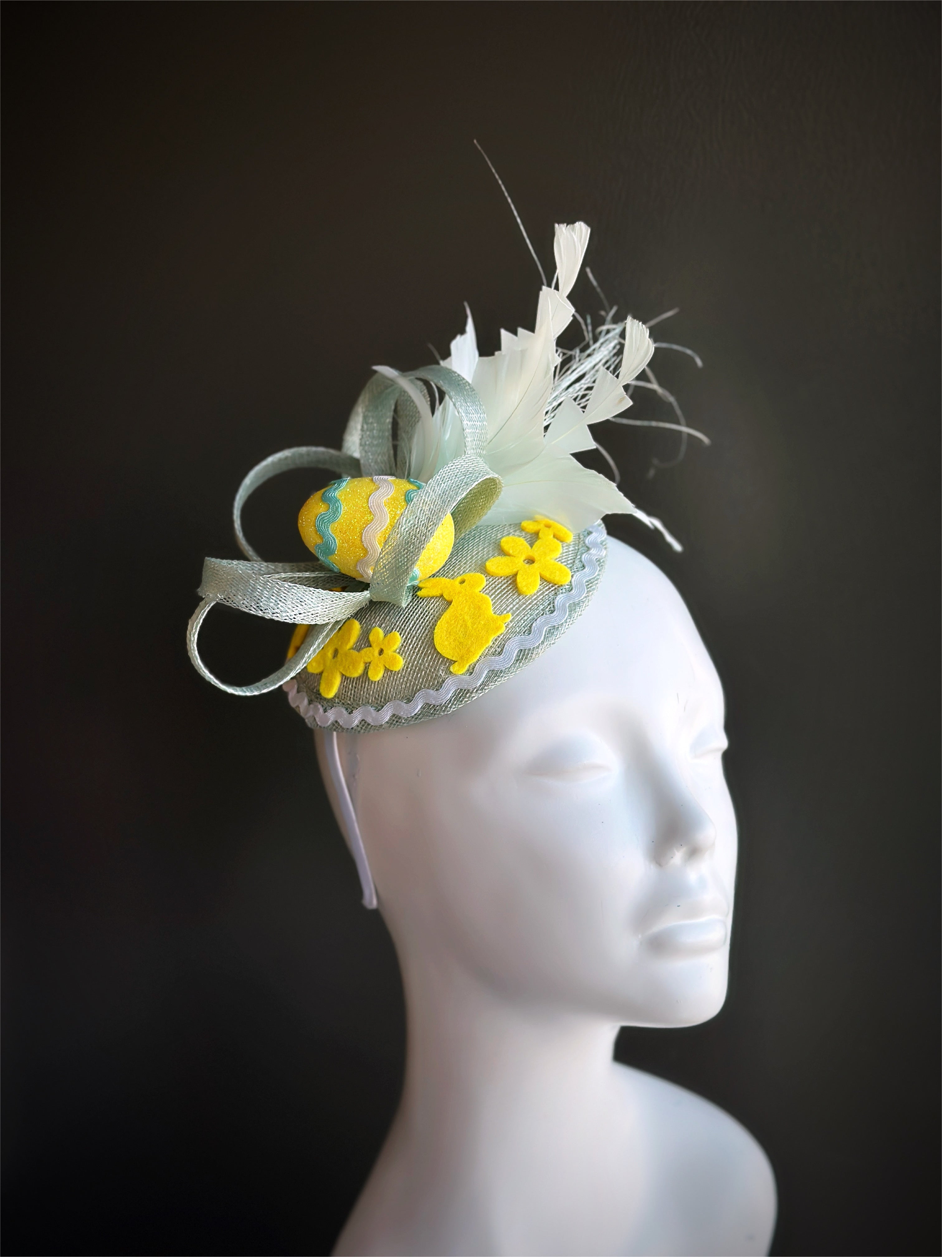 Pastel Easter fascinator hat with feathers, decorative egg, and floral details.