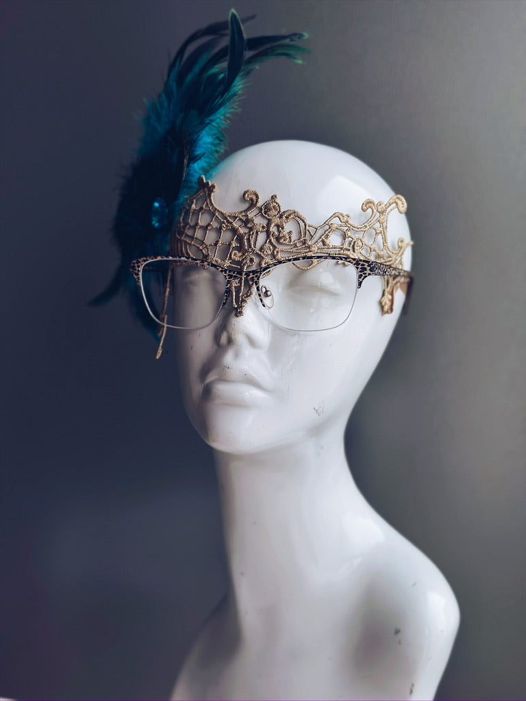Gold lace eyeglass mask with peacock feather and teal gem, designed for eyeglass wearers.