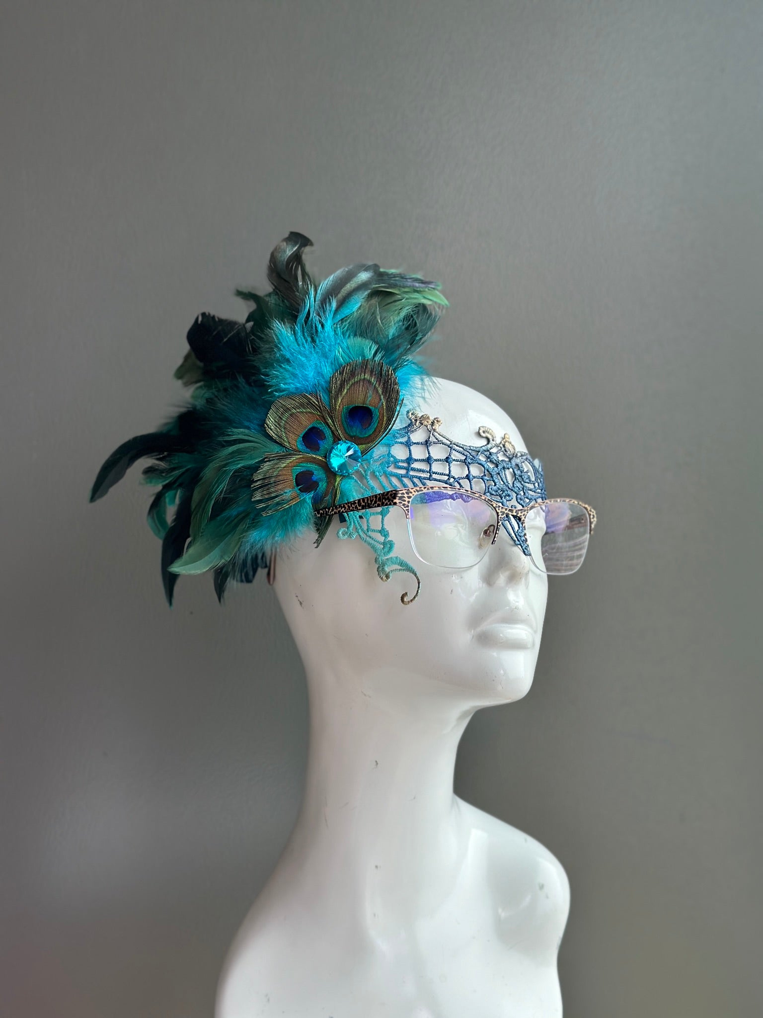 Eyeglass mask with teal lace, peacock feathers, and jeweled accents for a glamorous and comfortable masquerade look.