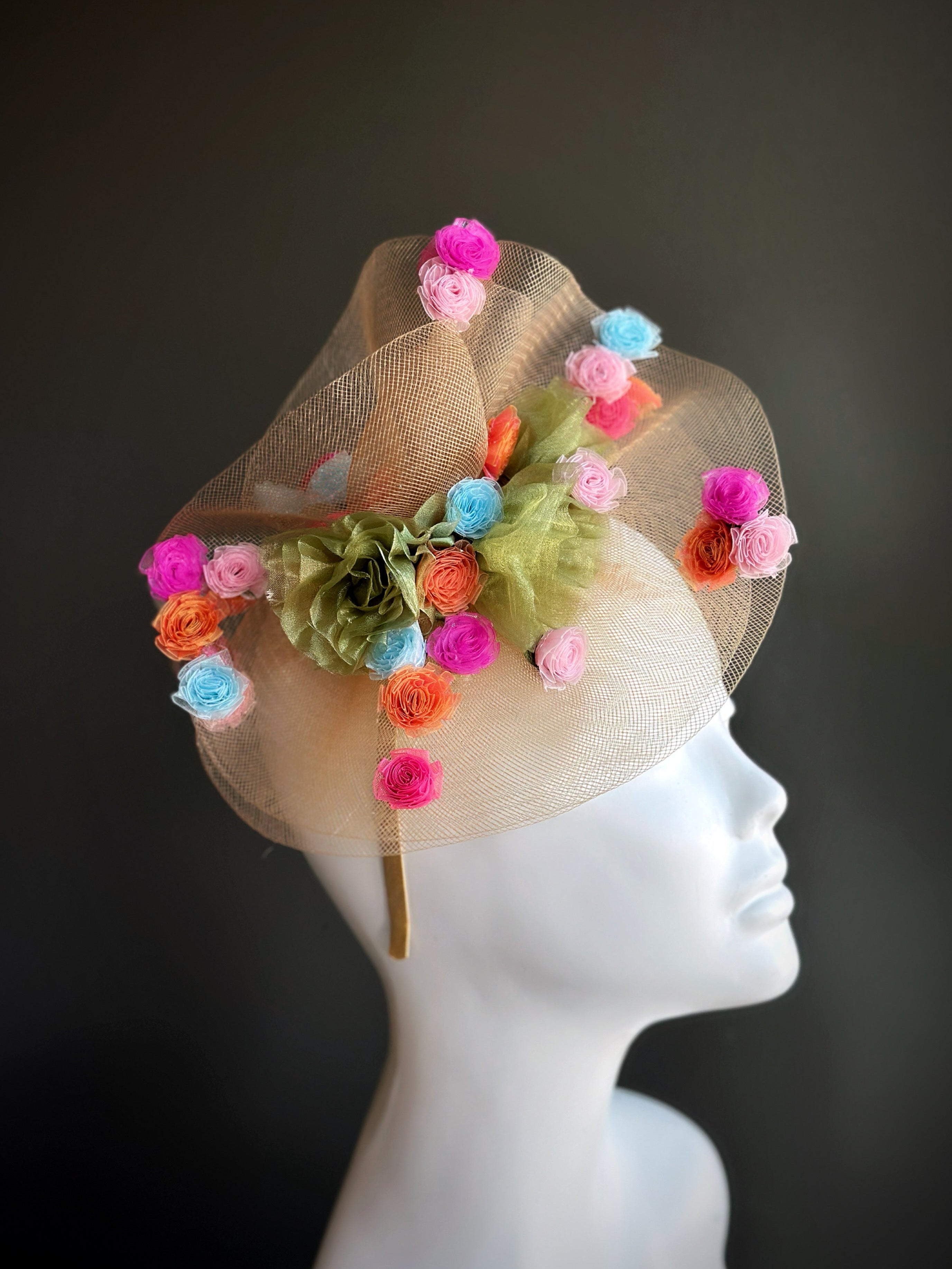 Fascinator hat with pastel rosettes, tulle, and green floral accents.