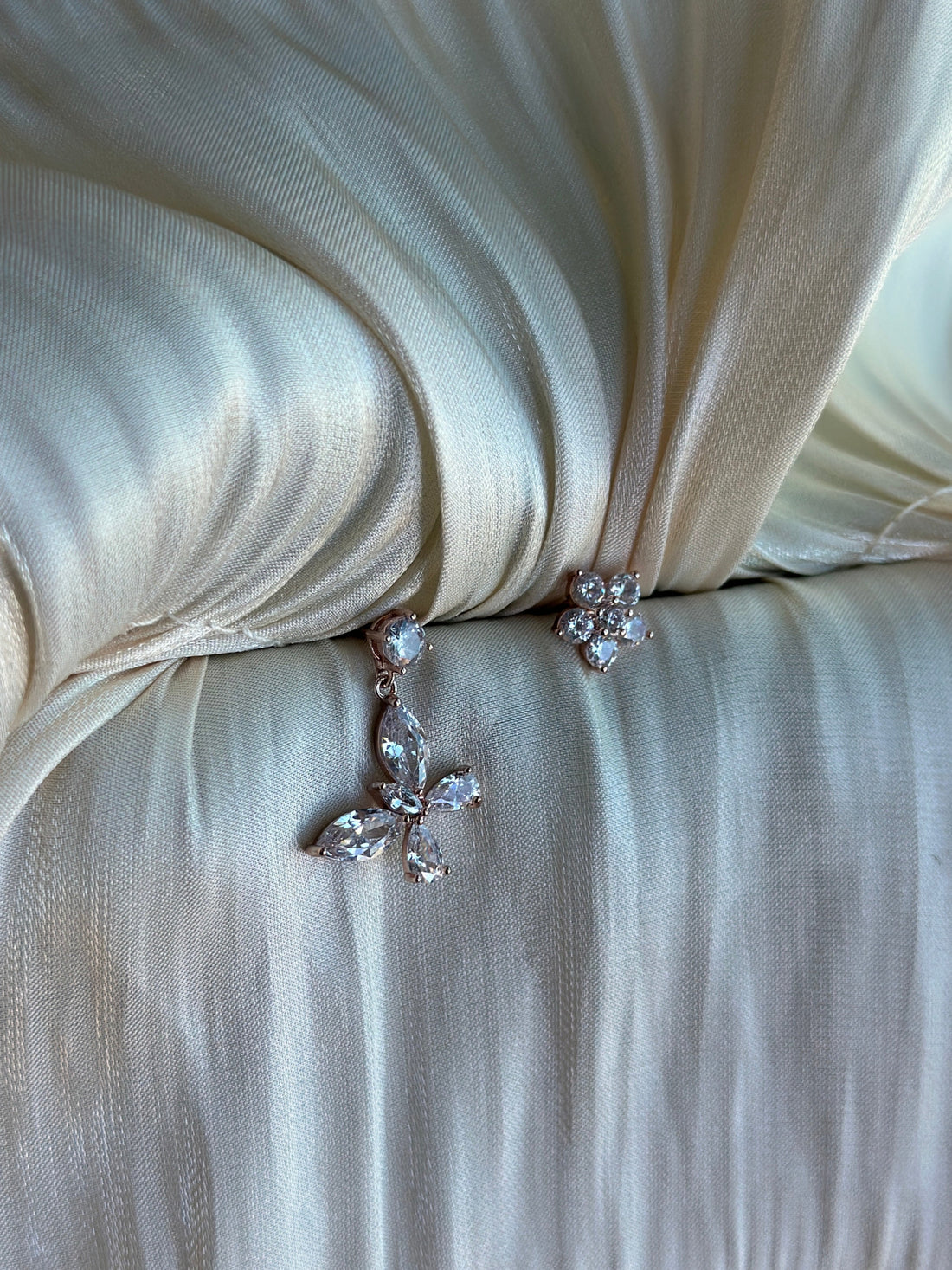 Rose gold butterfly and flower earrings on ivory satin fabric