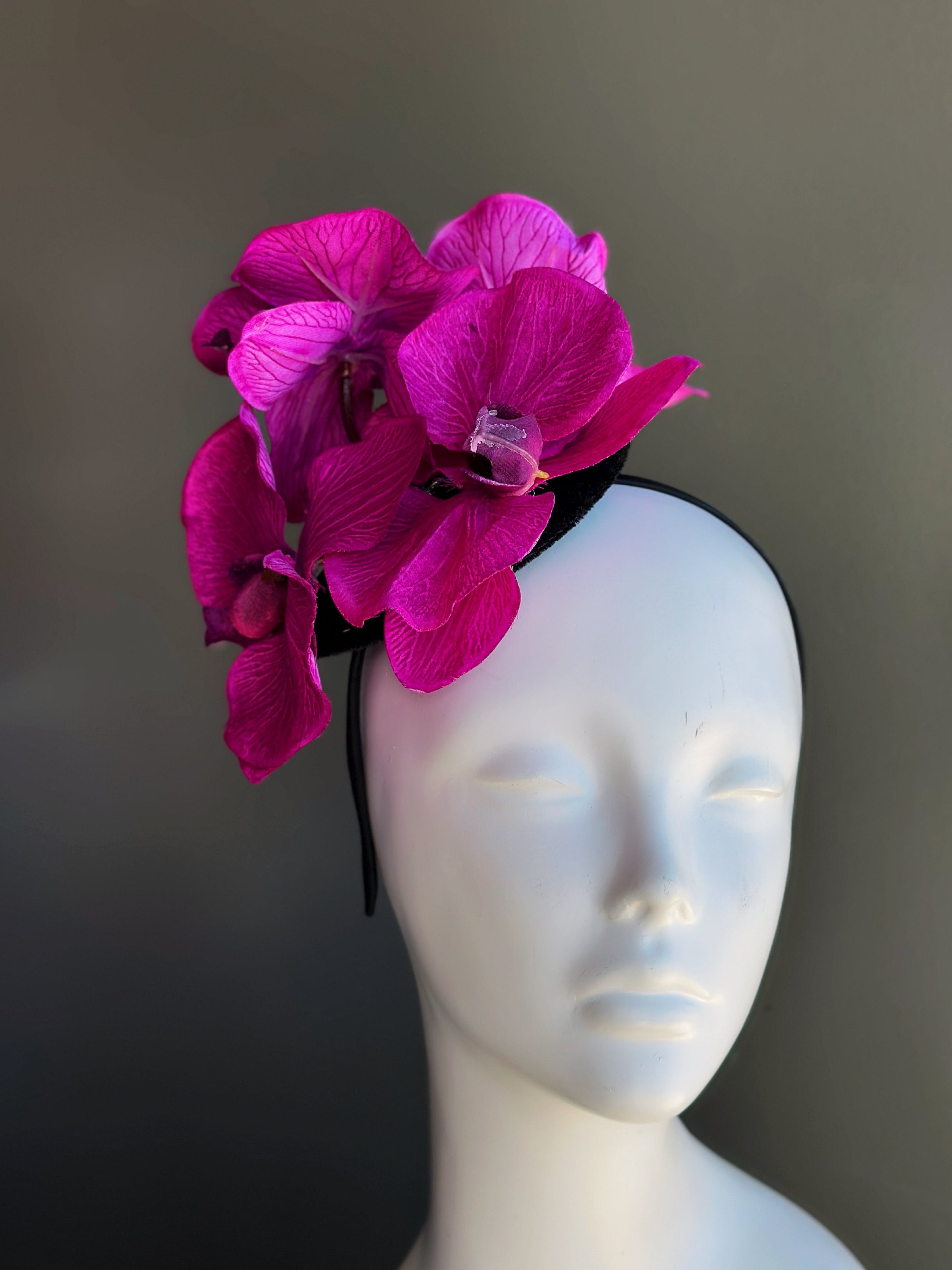 Fascinator hat with large blooming fuchsia orchids on a black base
