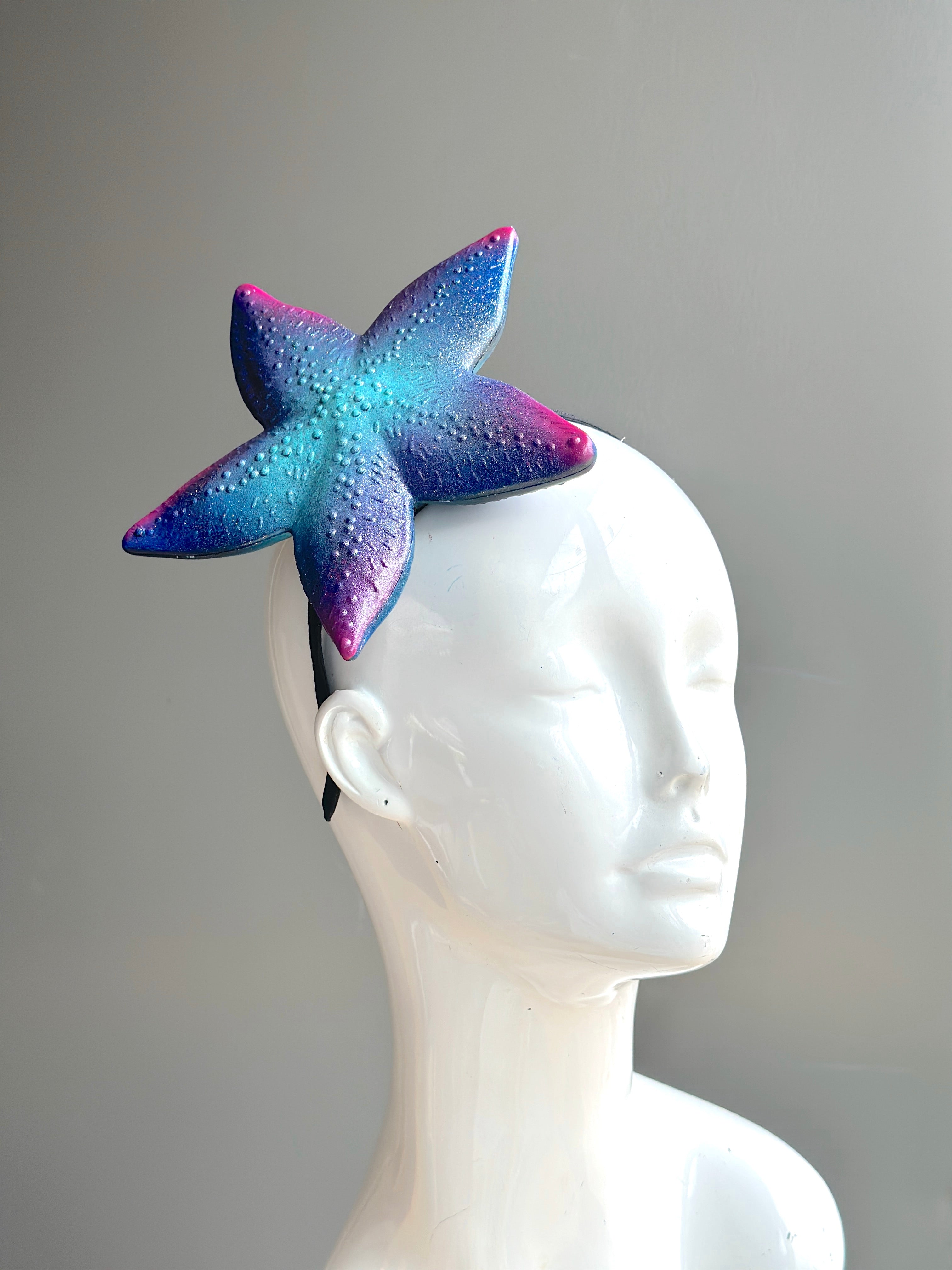 A shimmering starfish fascinator in cosmic shades of blue, purple, and pink, mounted on a headband—perfect for ocean and fantasy-themed events.