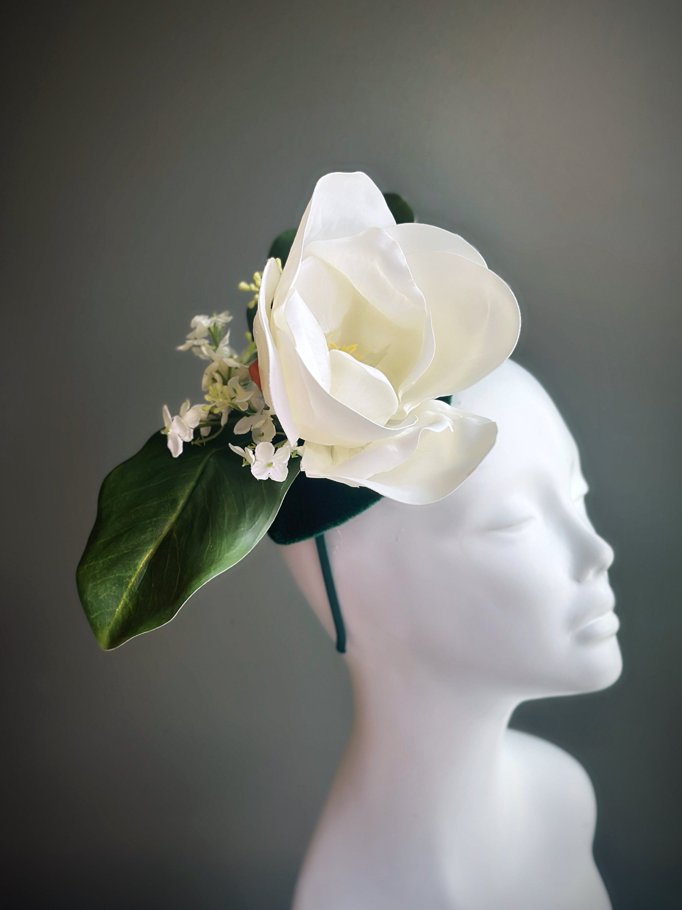 Elegant white fascinator hat with dramatic sculptural flowers and greenery