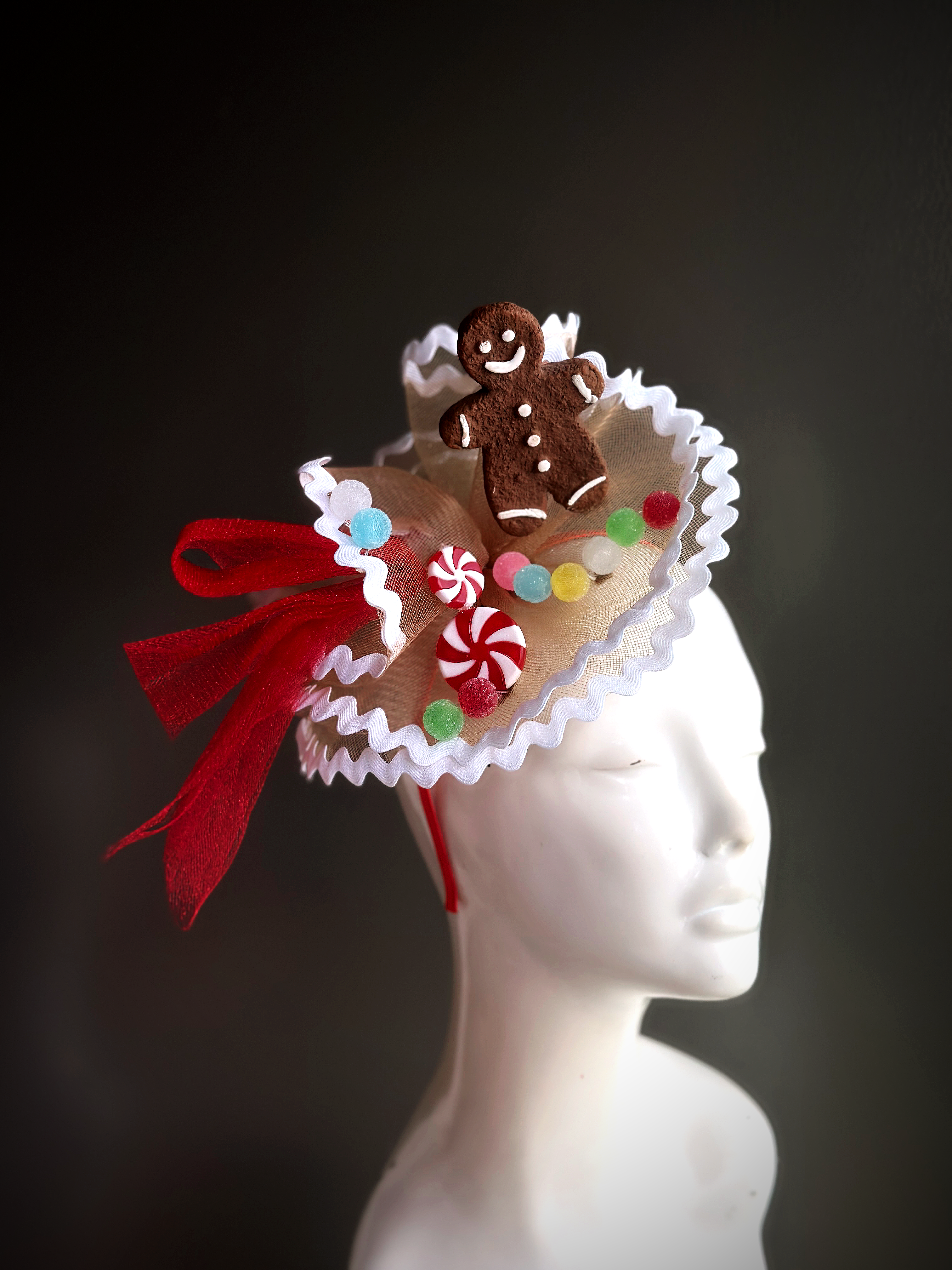 A delightful fascinator featuring a smiling gingerbread man, colorful candy accents, and festive red ribbon. Perfect for holiday parties and celebrations.
