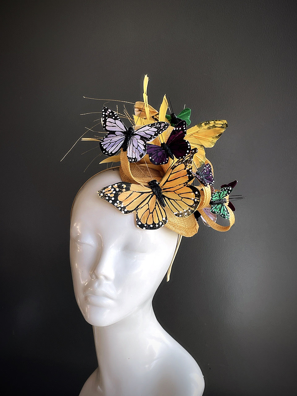 Gold fascinator headpiece with decorative butterflies in various colors displayed on a mannequin head.