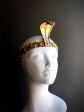 Gold cobra headpiece with intricate detailing, inspired by Ancient Egyptian serpent designs, displayed on a white mannequin