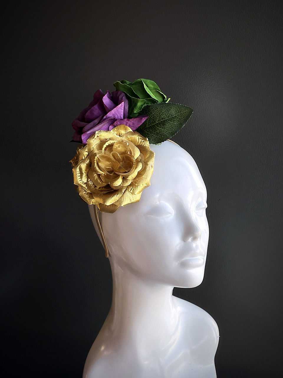 Gold and purple rose fascinator displayed on a mannequin head with a gold fascinator hat base.