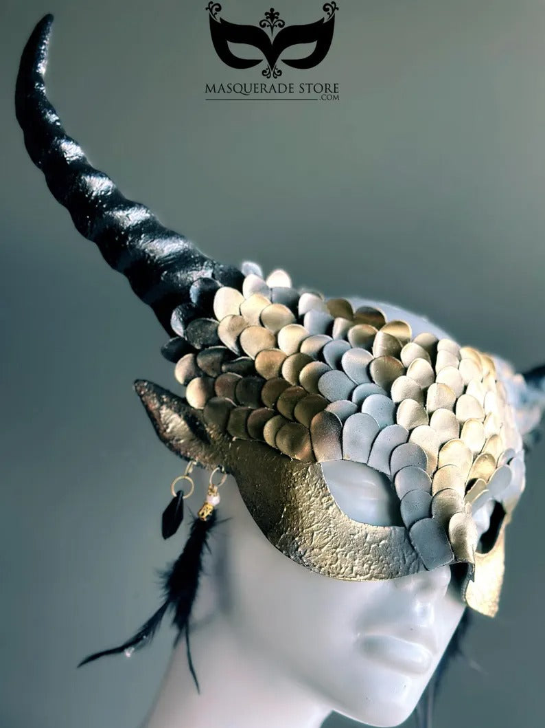 Fantasy dragon horn masquerade mask in gold with scales, black horns, and feather accents, designed as a dramatic headdress.