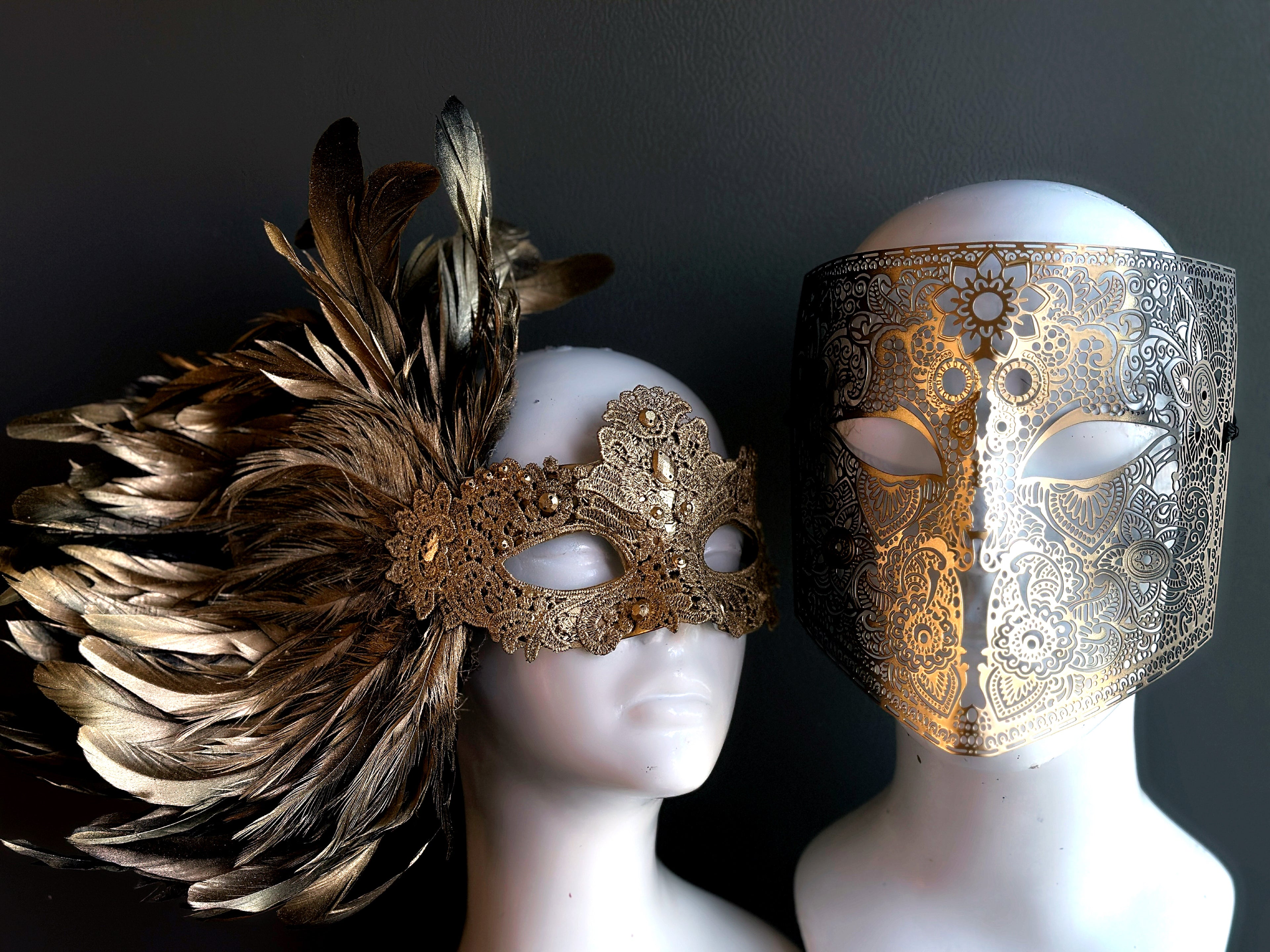 Luxurious gold lace feather mask paired with an ornate full-face filigree mask, ideal for masquerade balls and formal celebrations.
