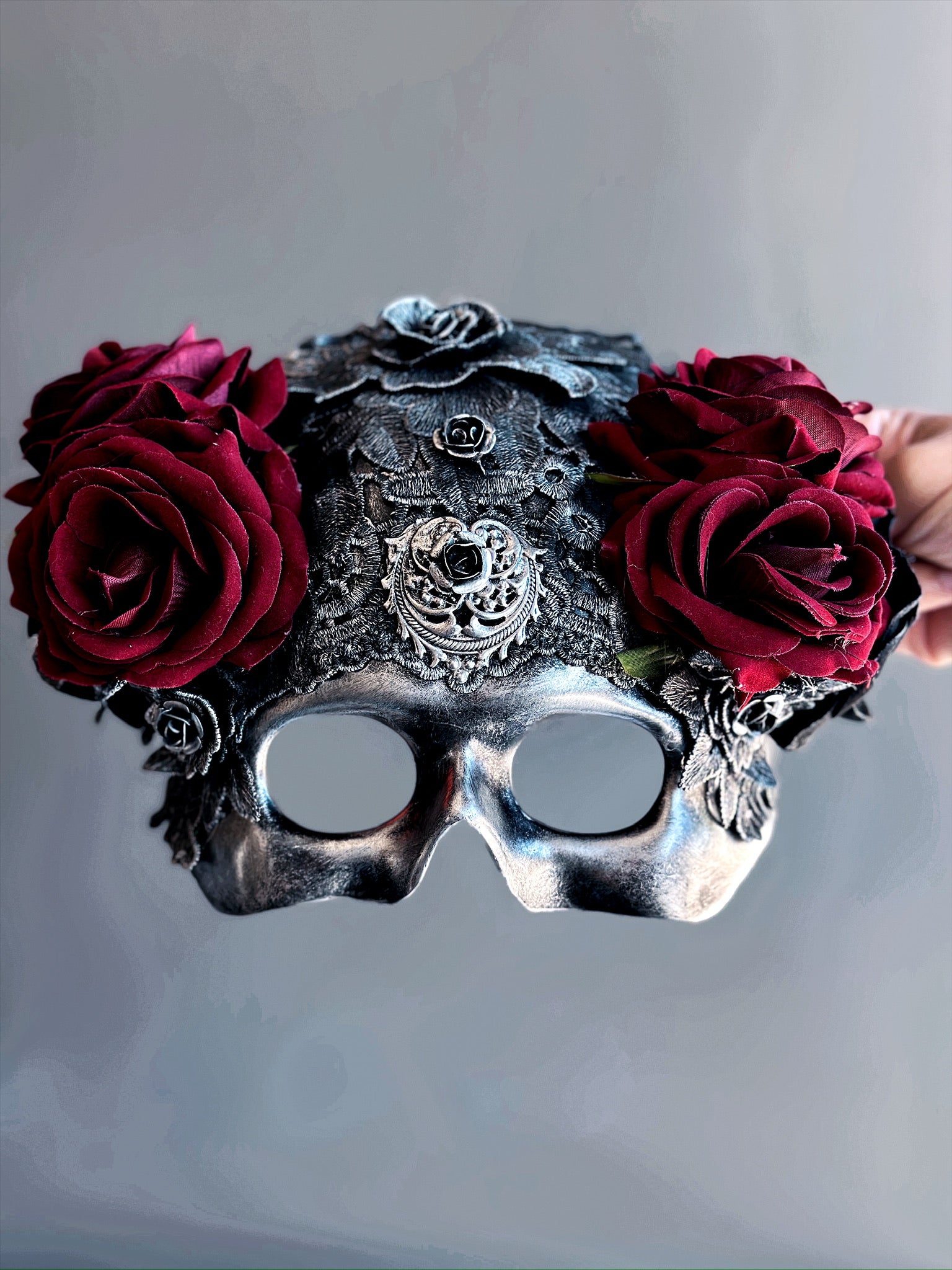 Skull-shaped masquerade mask with red roses, black lace, and silver filigree