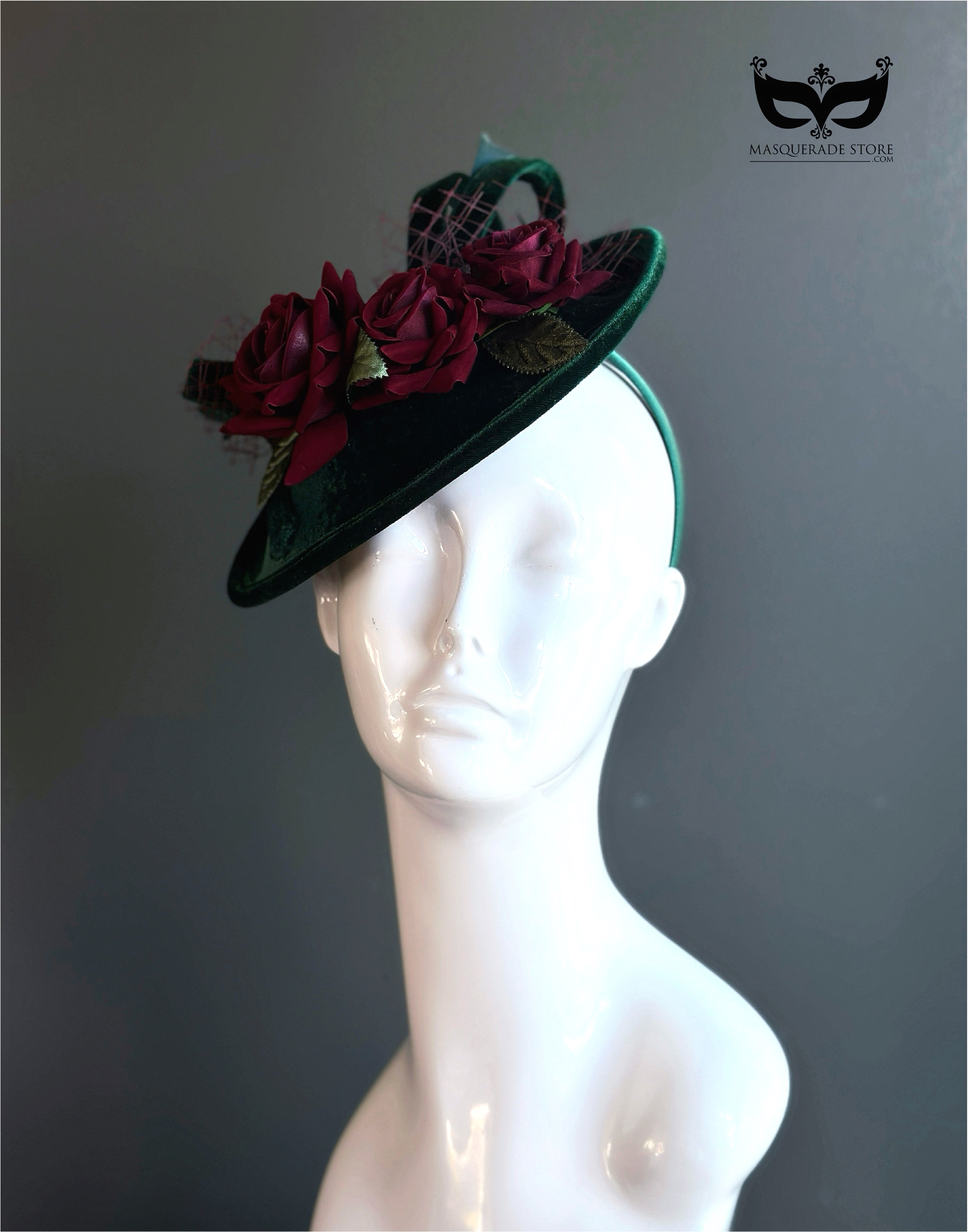 Green velvet fascinator hat with red floral accents.