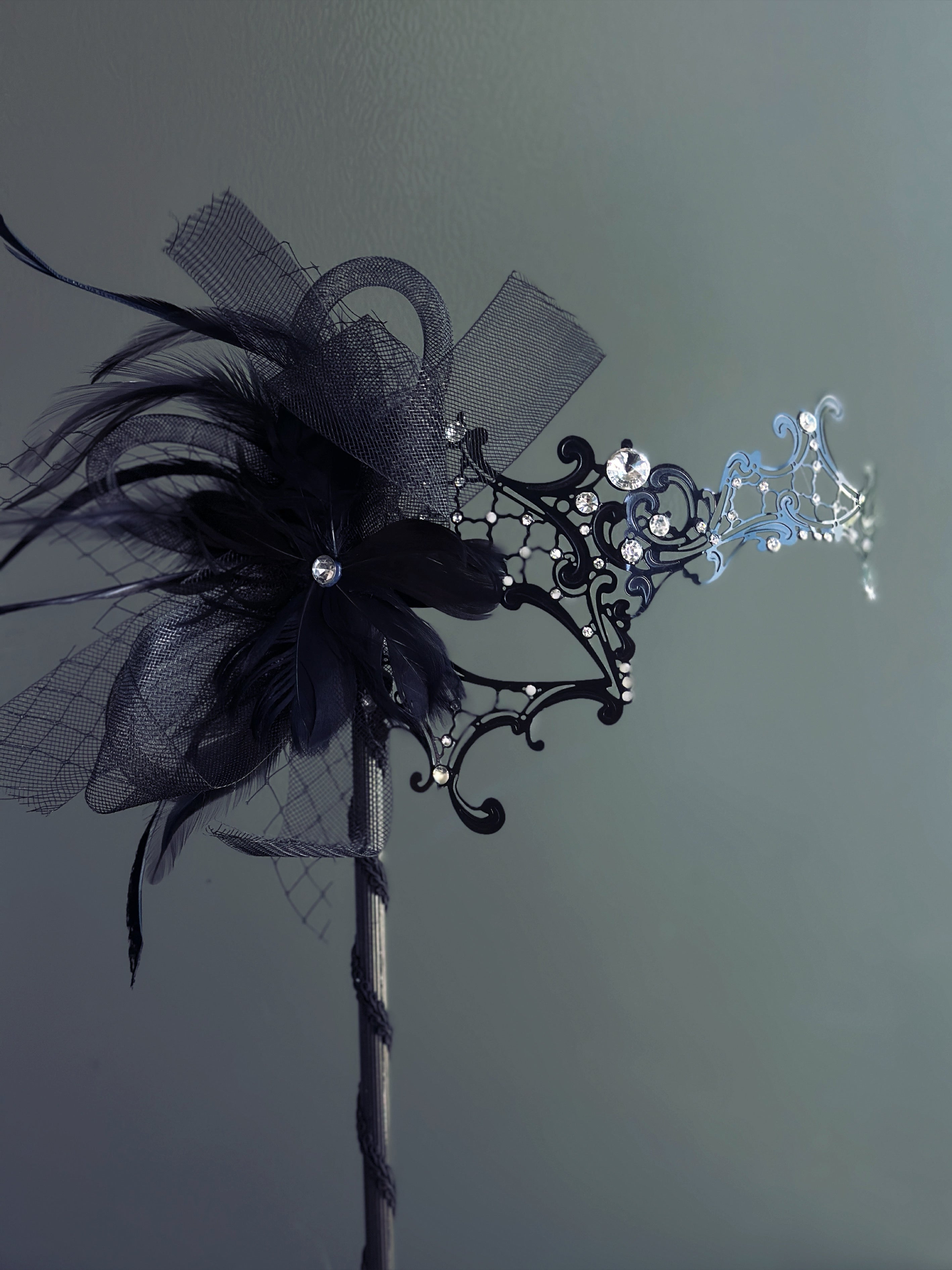 Handheld black masquerade mask with black feathers and rhinestone accents