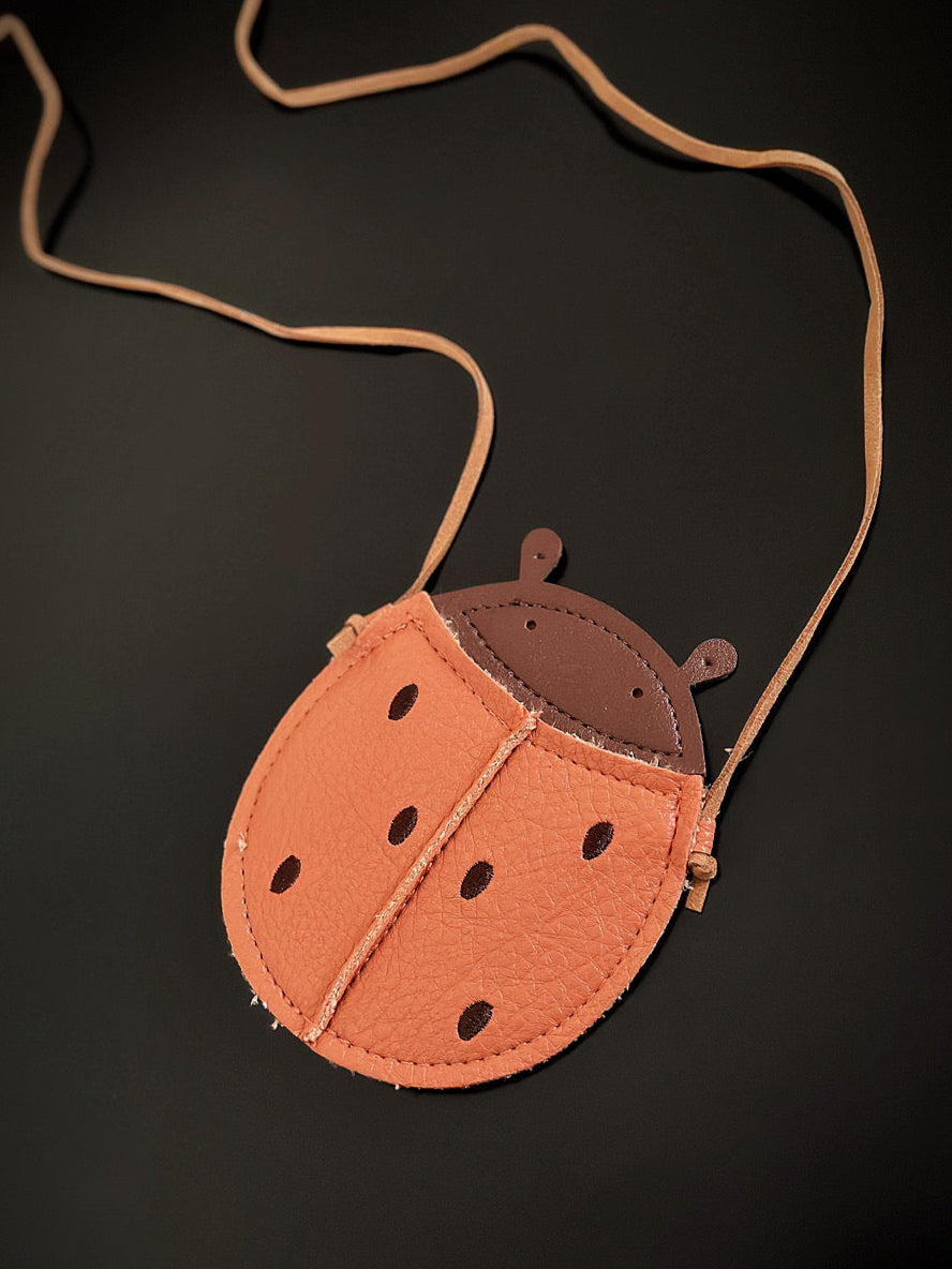 Kids ladybug-shaped mini crossbody bag with tan strap and stitched faux leather in orange and brown.