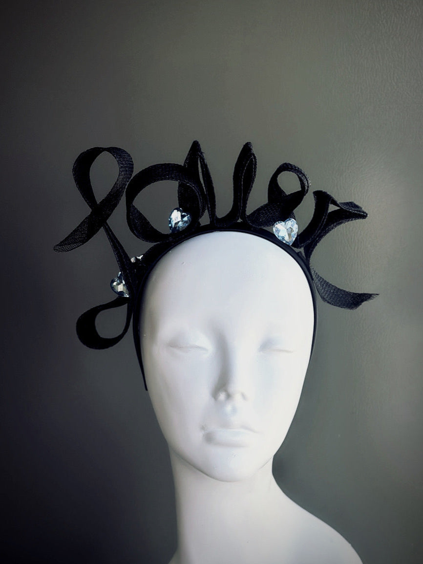 Black fascinator hat with "Lover" spelled in sinamay ribbon and crystal accents