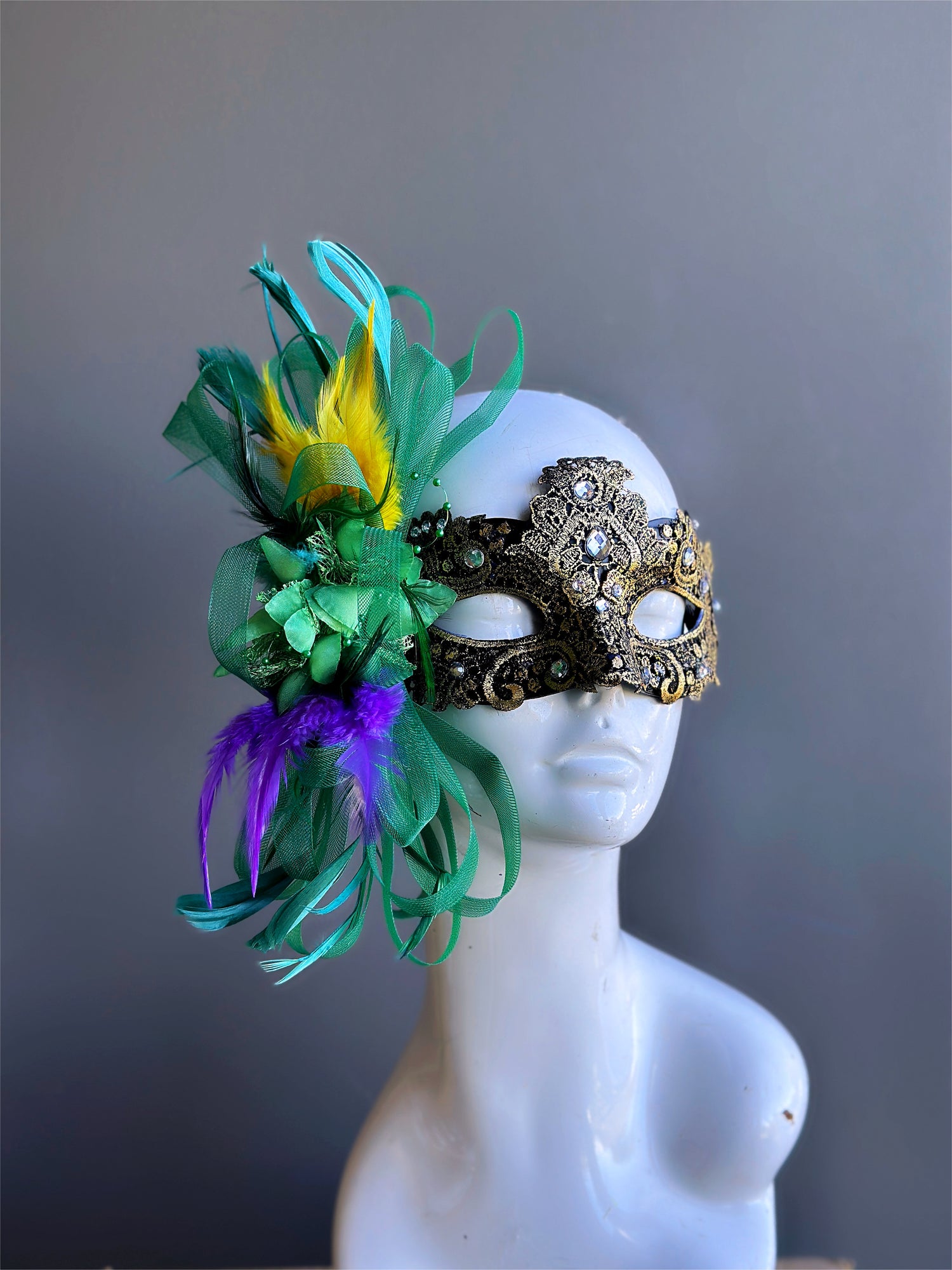 Gold Mardi Gras masquerade mask for women with green floral ribbons and yellow, purple, and green feathers.