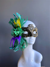 Gold Mardi Gras masquerade mask for women with green floral ribbons and yellow, purple, and green feathers.